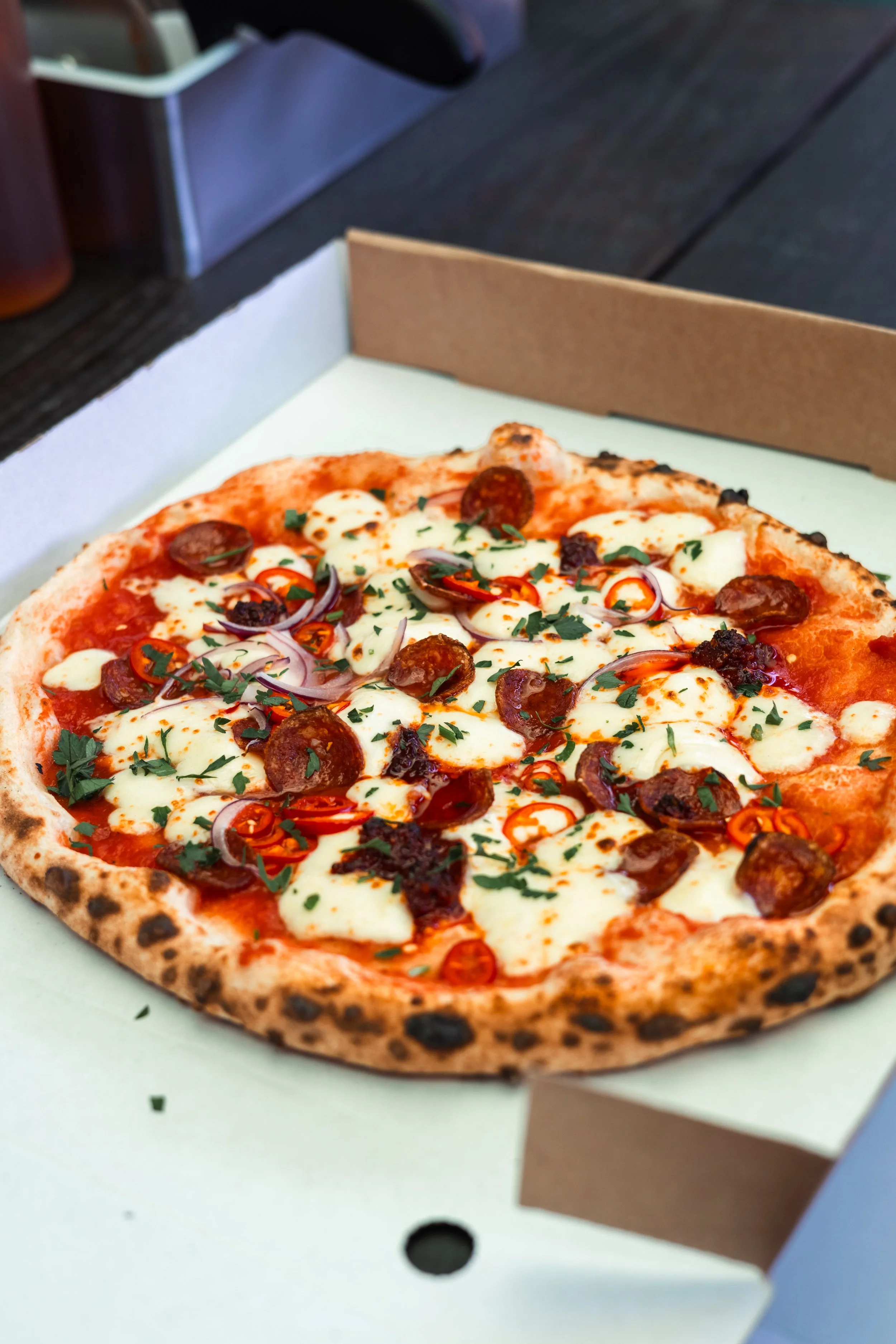 Fresh pizza with pepperoni, cheese, sliced red peppers, onions, and parsley in a cardboard pizza box.