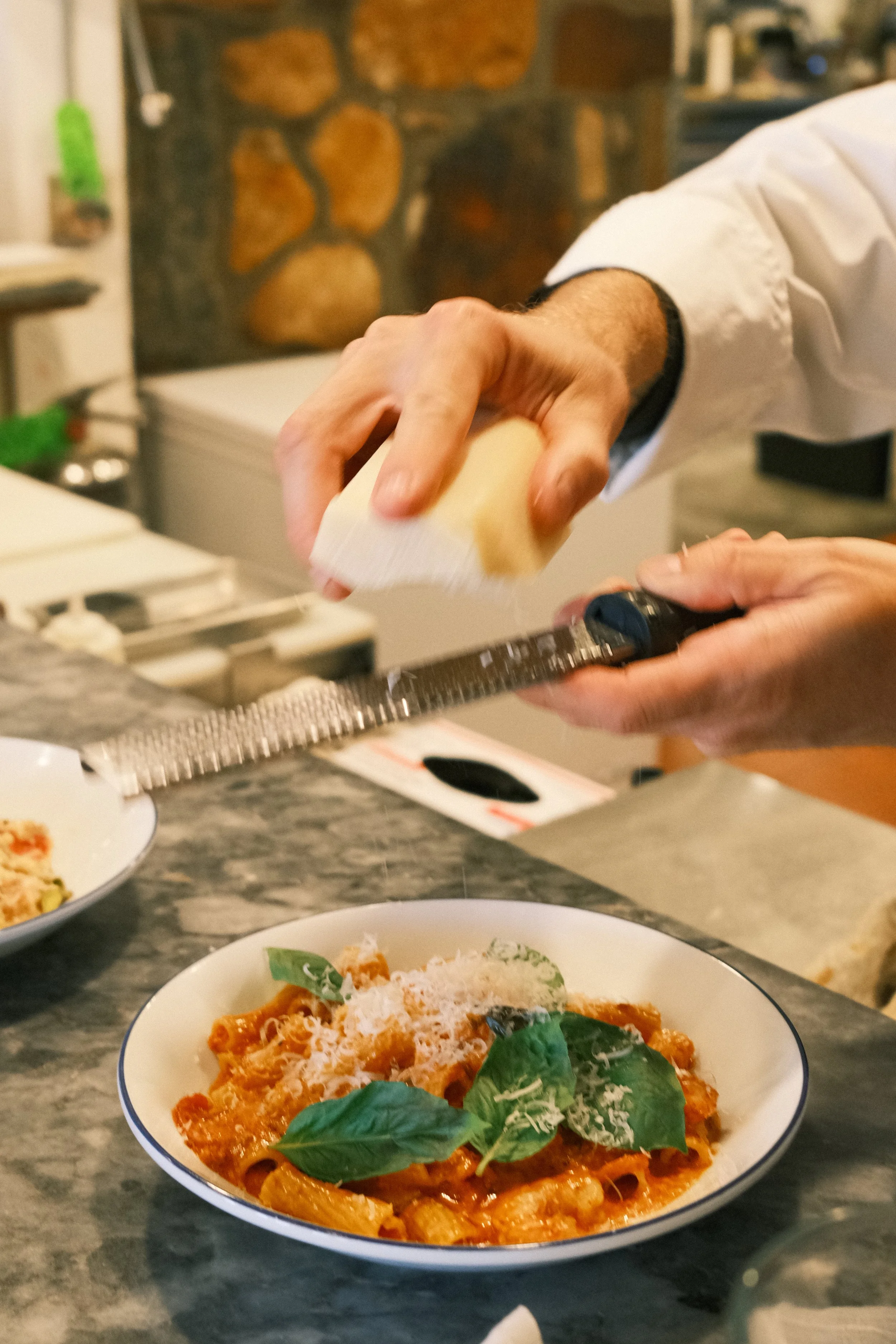 Chef grating cheese over a plate of baked pasta with basil leaves and grated cheese.