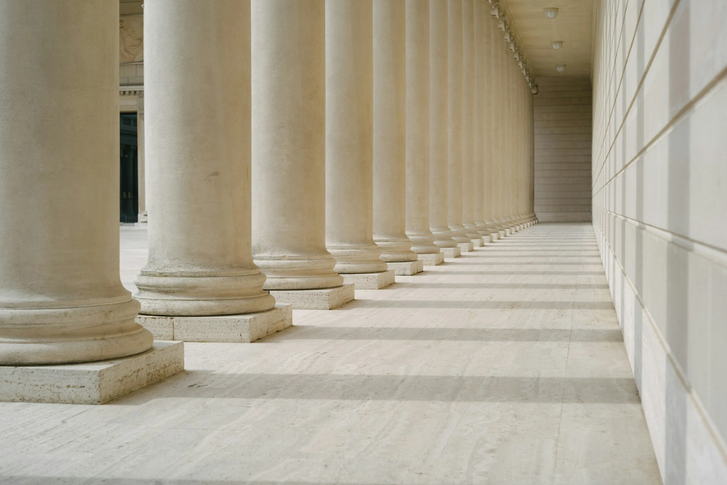 A row of classical stone columns with shadows cast on the floor.