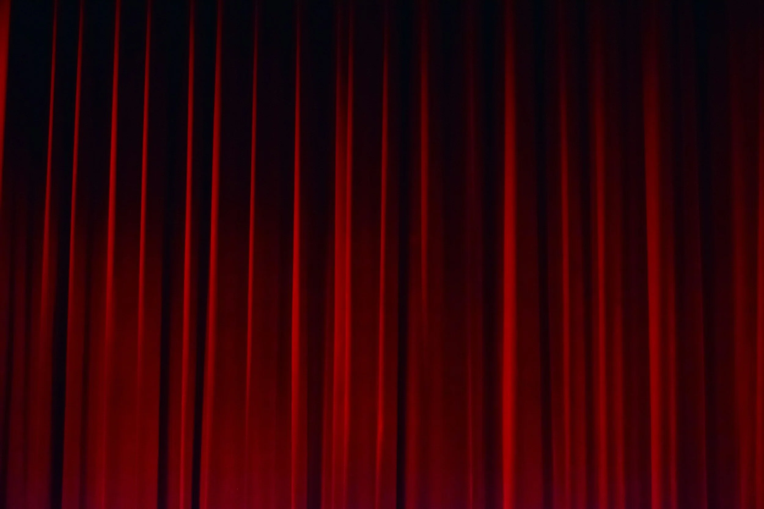 Red stage curtain closed, with vertical folds.