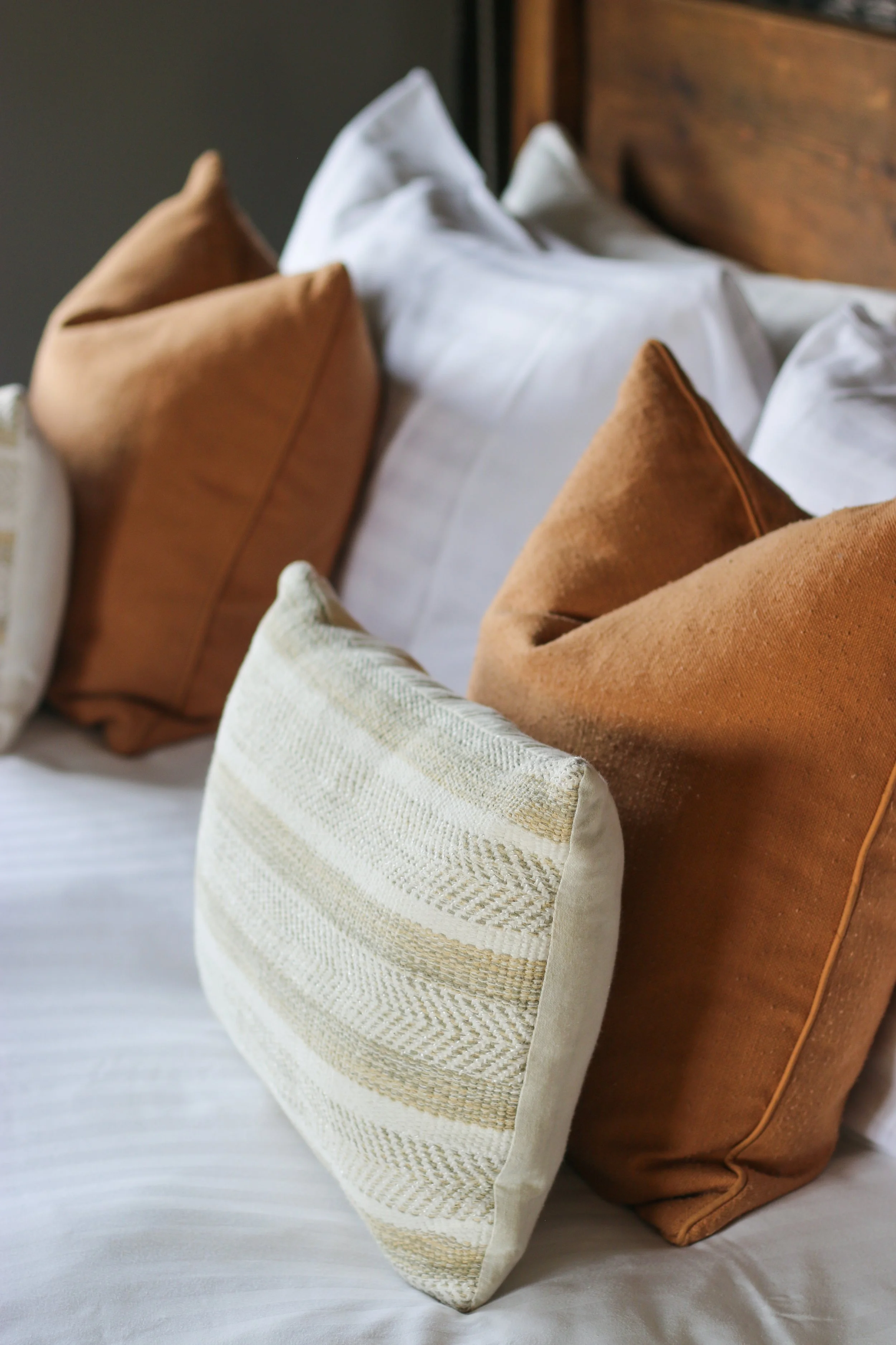 Collection of decorative throw pillows in neutral tones on a bed with white sheets.