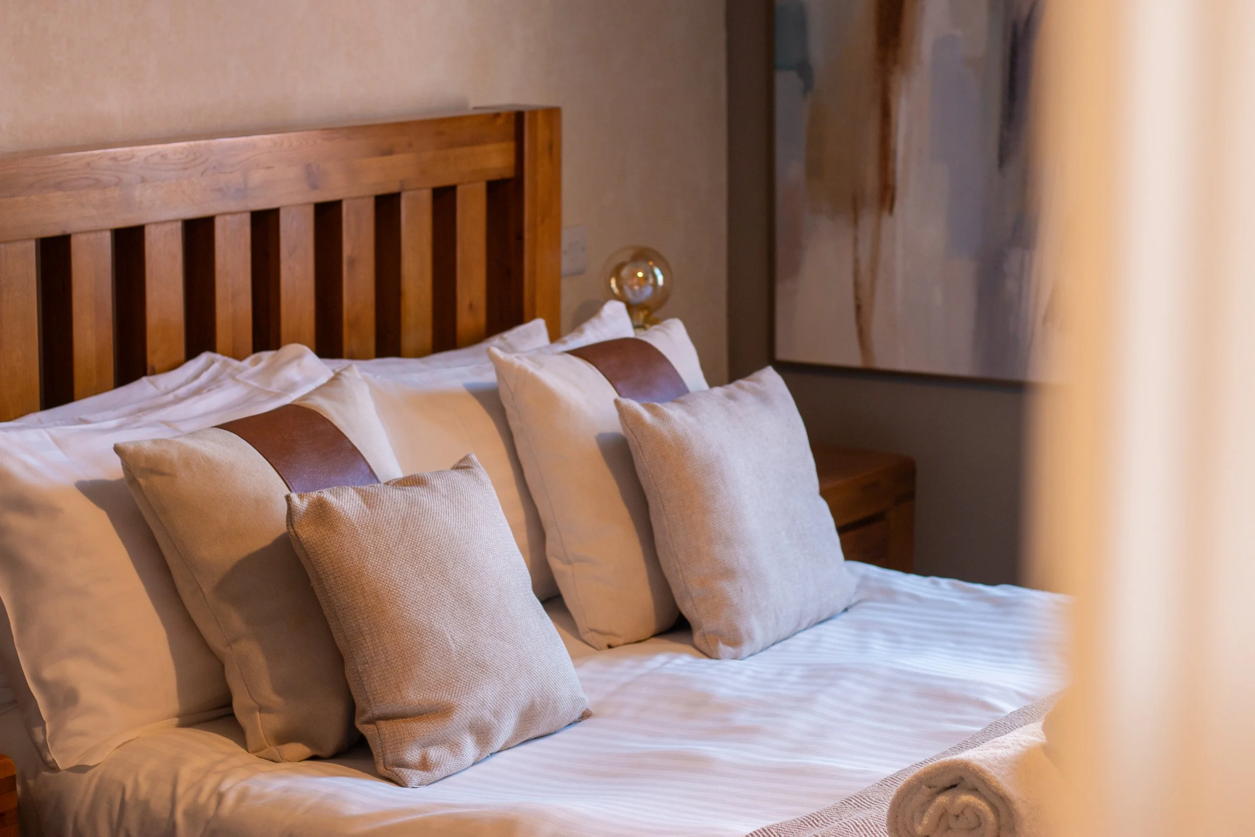 A neatly made bed with neutral-colored pillows and a wooden headboard in a cozy bedroom.