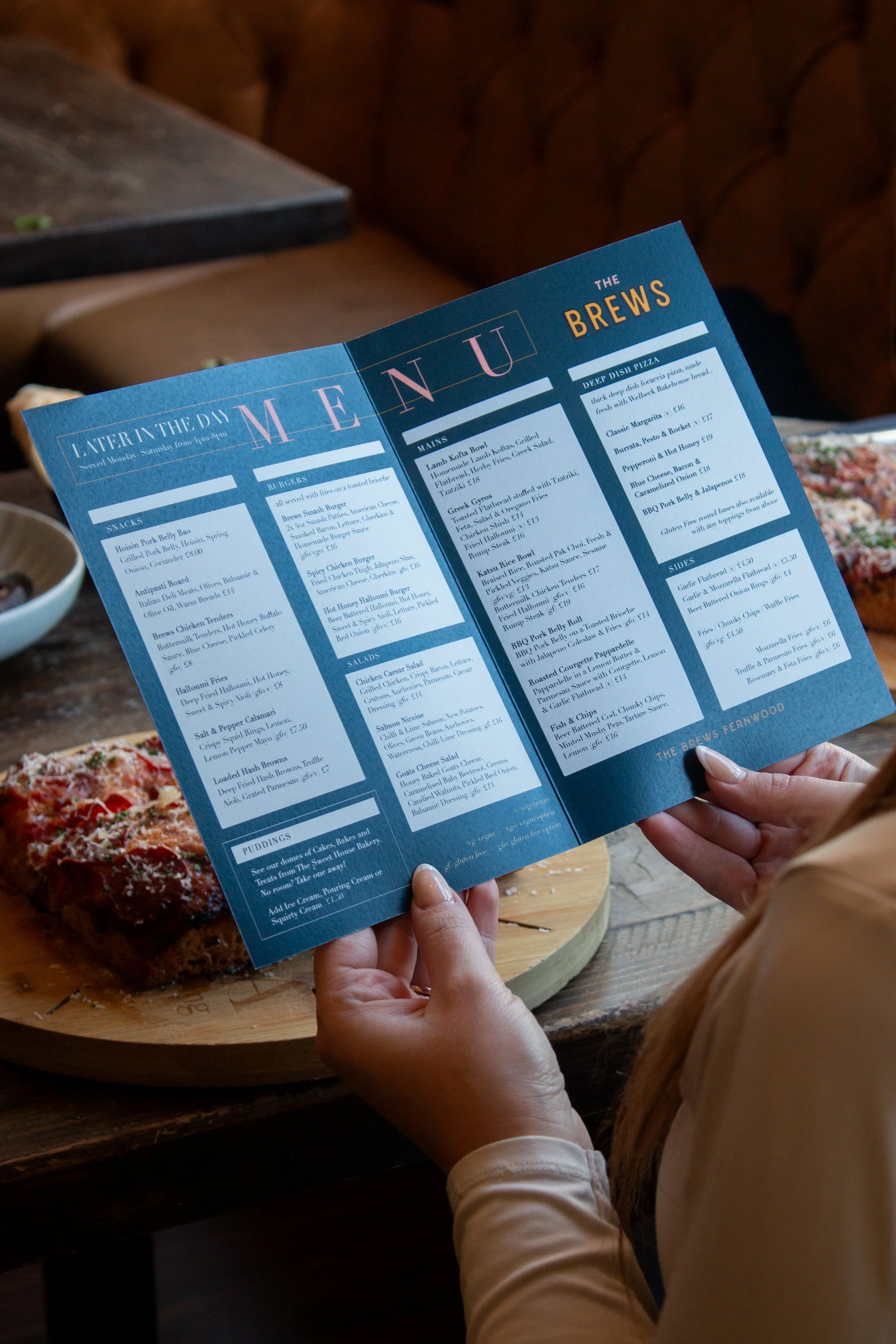 A person holding a blue restaurant menu with food options, and a plate of food on a wooden table.