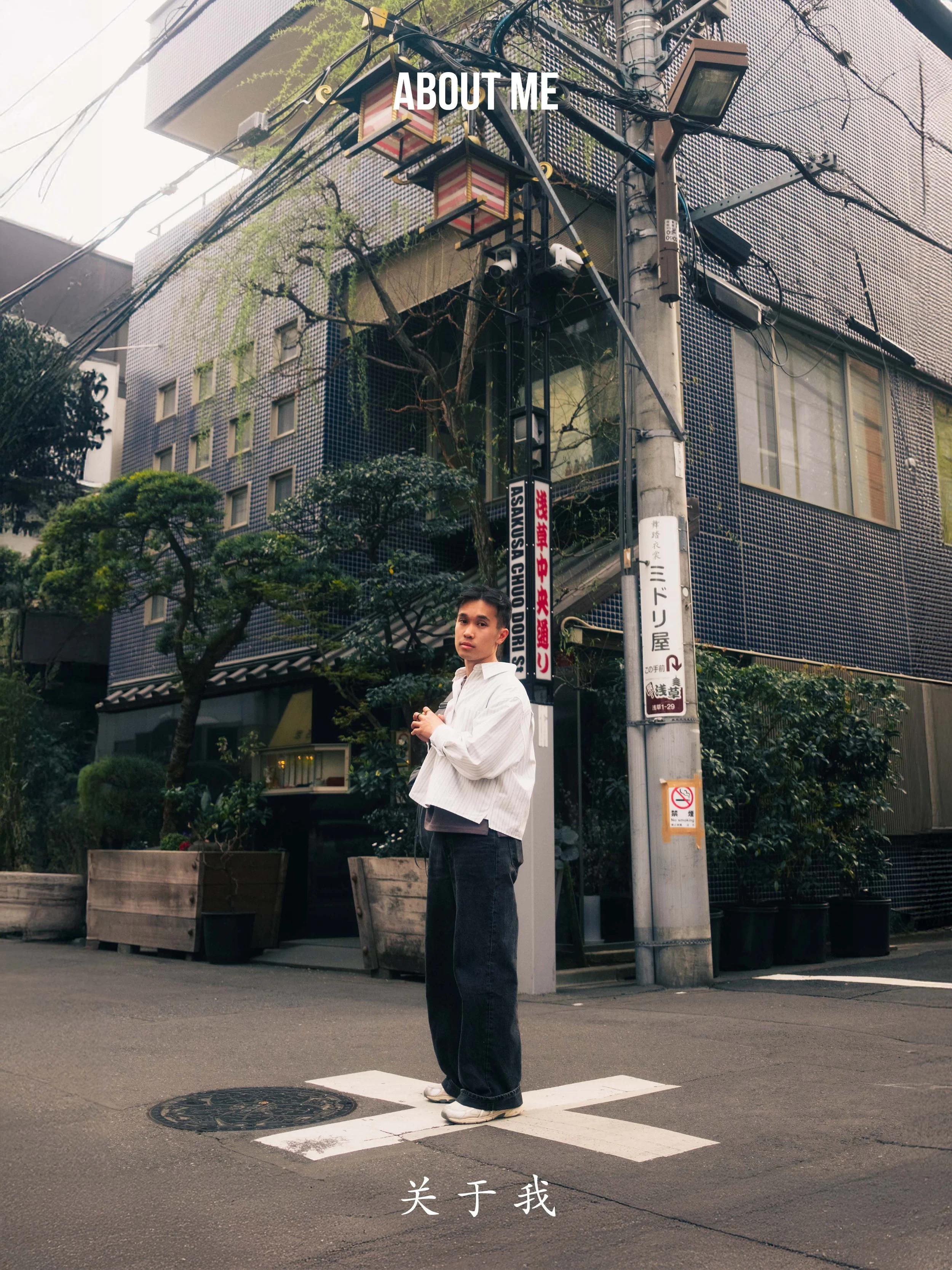 A young man standing on a crosswalk at an urban street corner with buildings, trees, and street signs in the background.