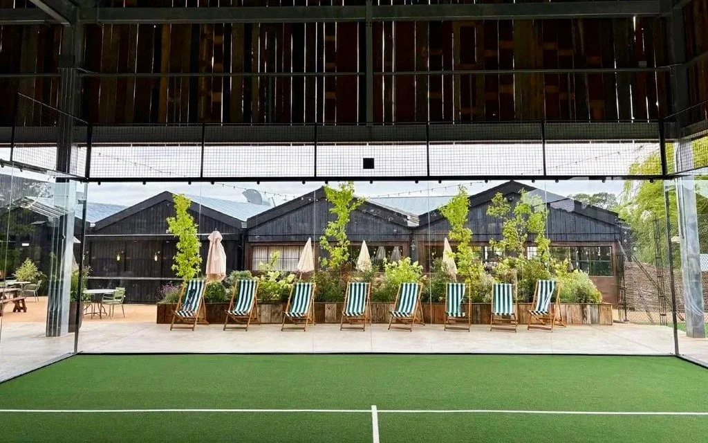 View of a patio area through the glass of a Padel Court at soho farmhouse