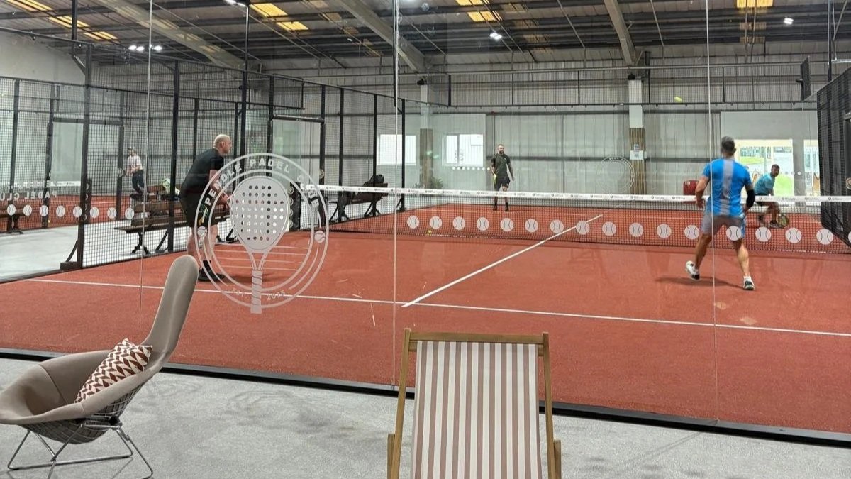 Indoor UK padel tennis court with four players, net, and glass walls.