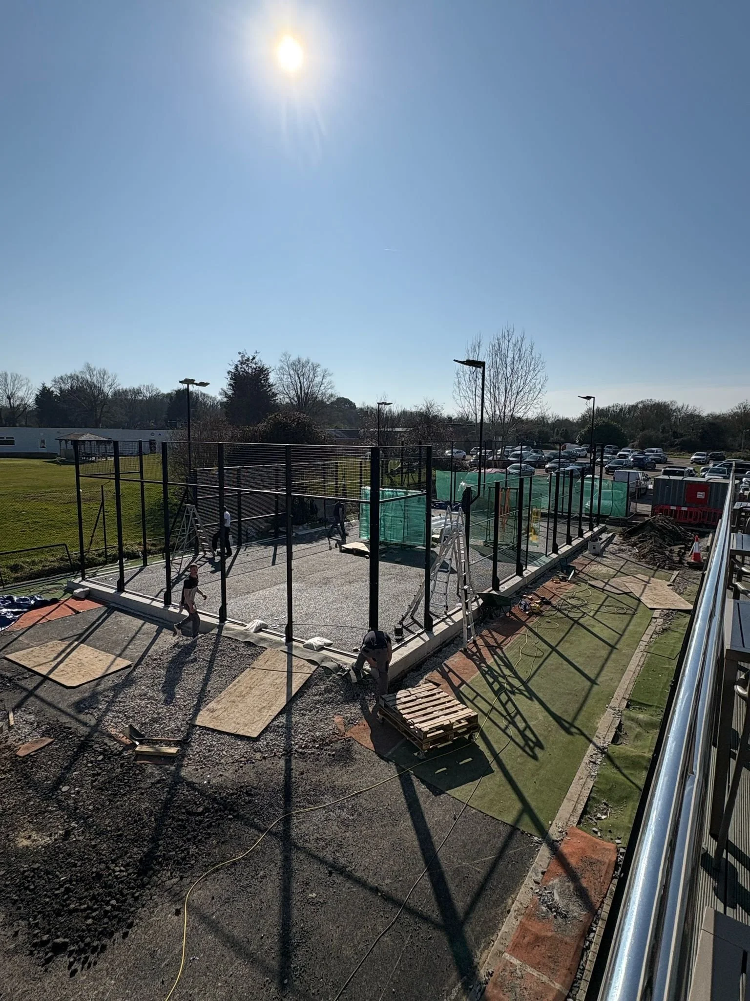 Construction workers building a Padel court outdoors, with gravel and paving materials, under a bright sunny sky.