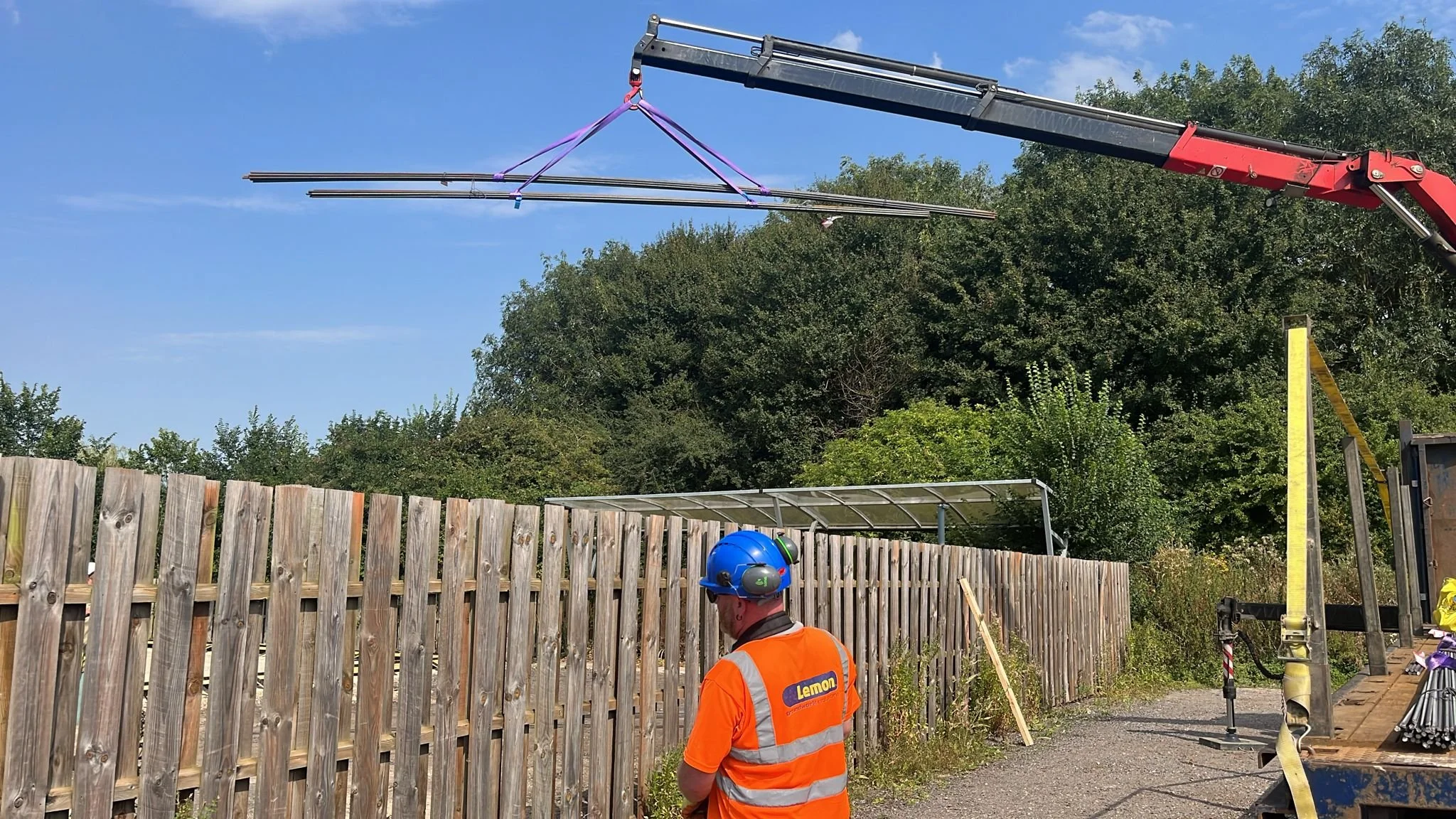 A construction worker Operating a HIAB lifting Padel Court Materials over a large fence at the University of Cambridge