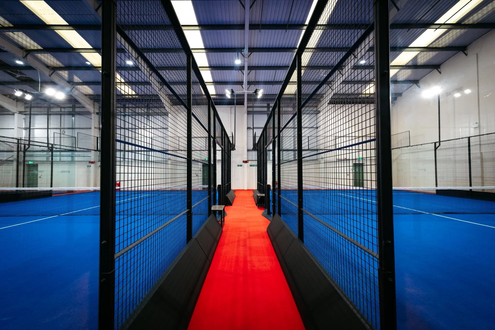 Indoor padel tennis court with blue playing surface surrounded by glass walls and black fencing UKs Best Padel