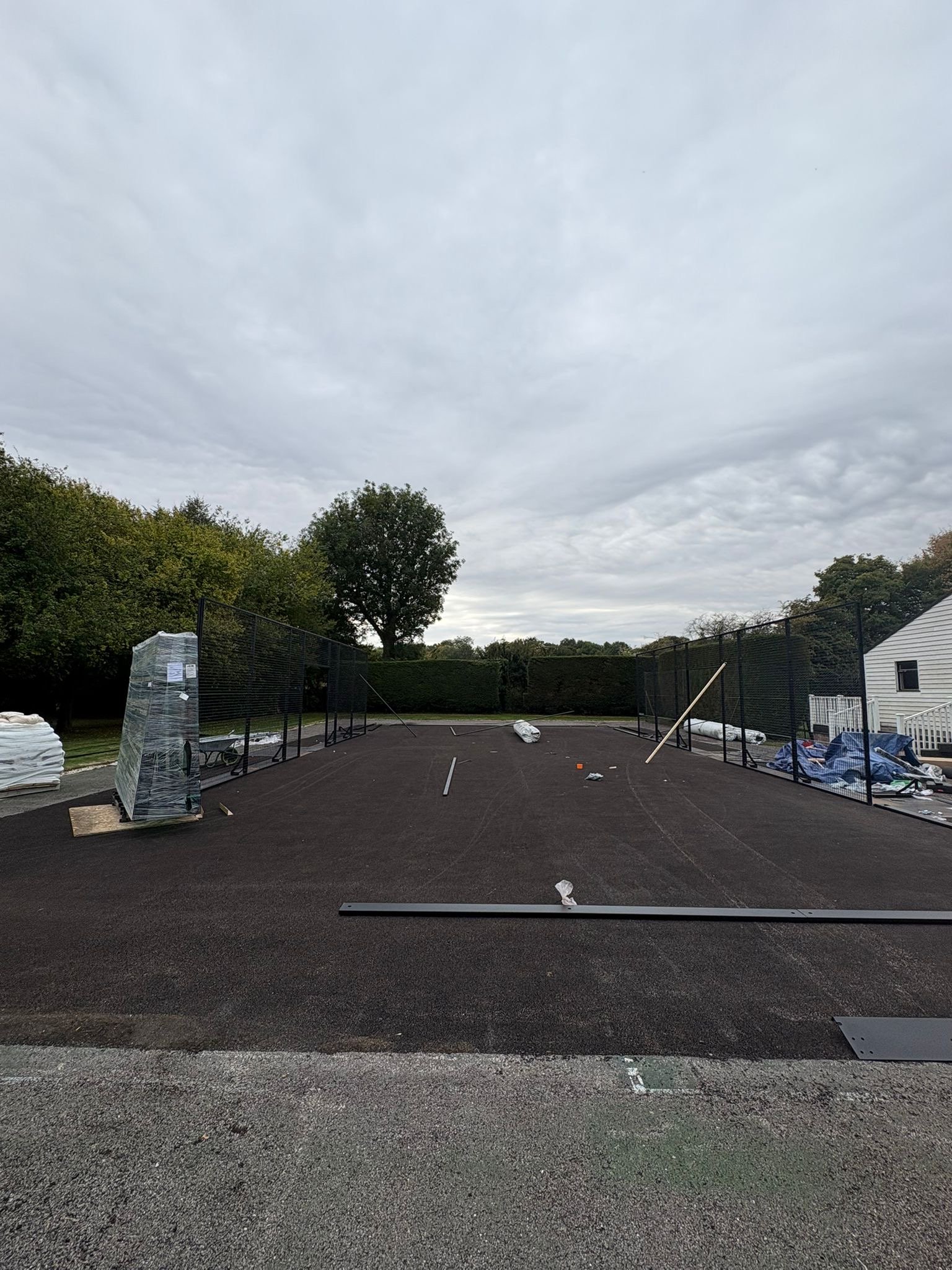 Construction site on a tennis court with fencing, construction materials, and tools. Tennis to Padel conversion in the UK