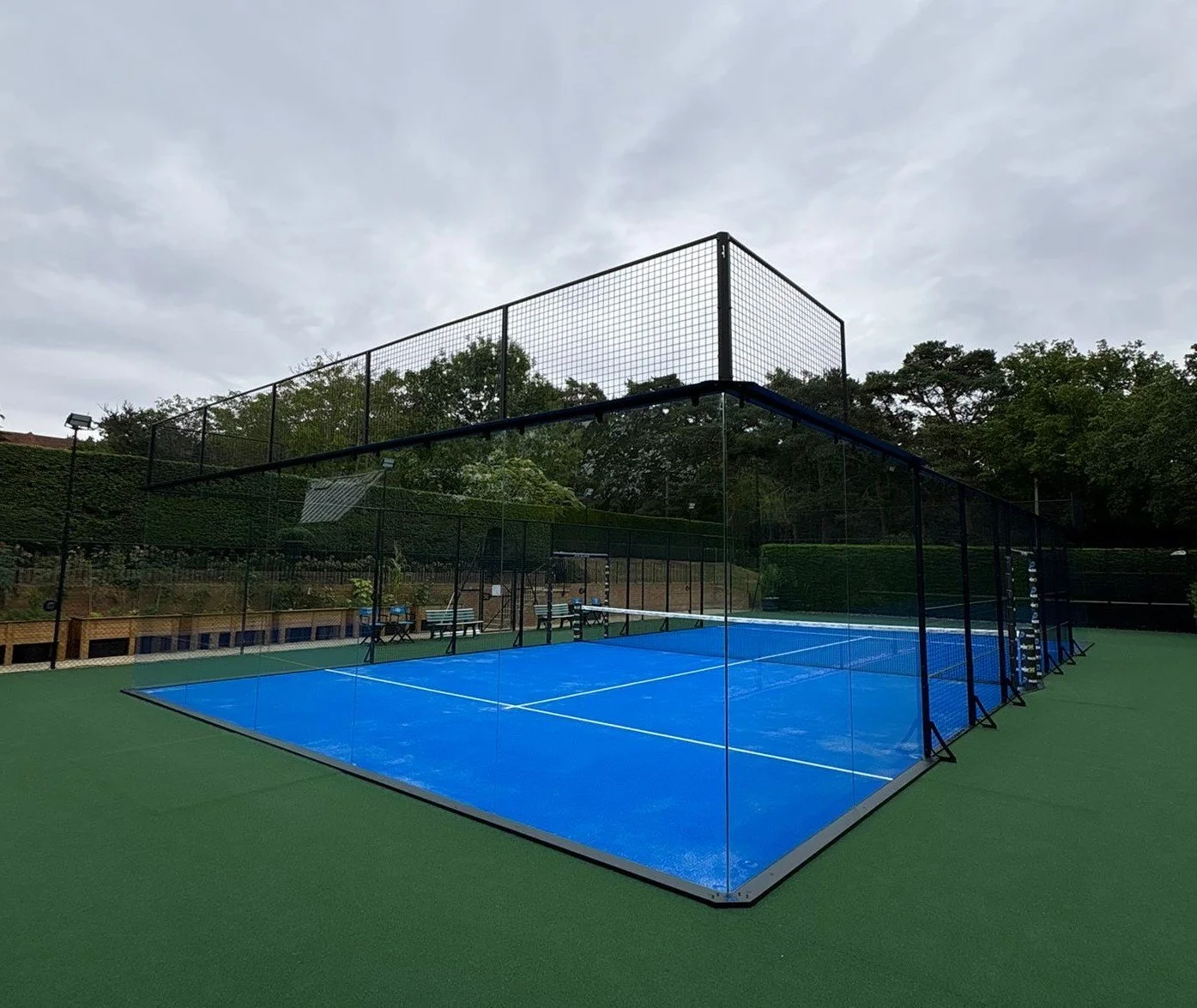 An outdoor padel tennis court with blue surface, Surrounded by green turf.