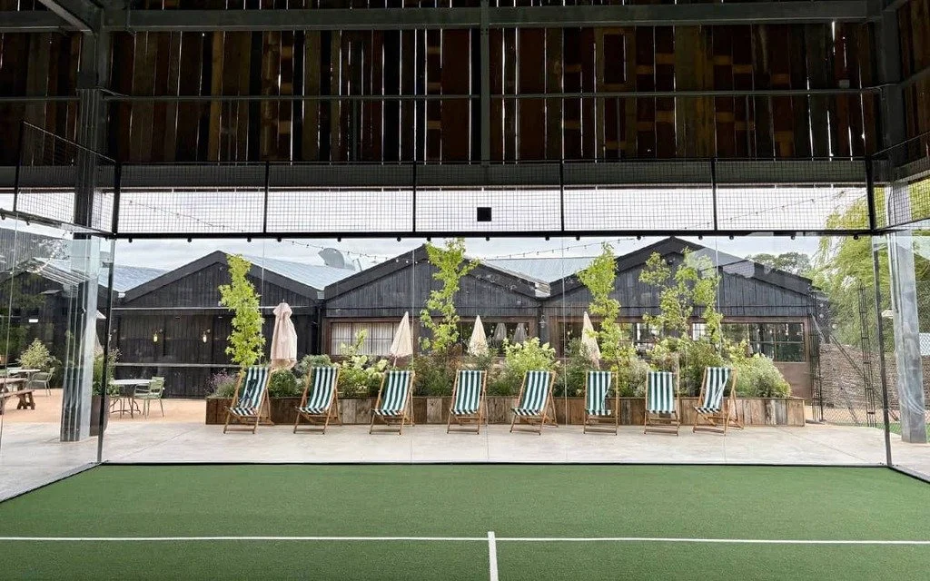A Padel Court underneath a Canopy overlooking a Patio with several sunbeds.