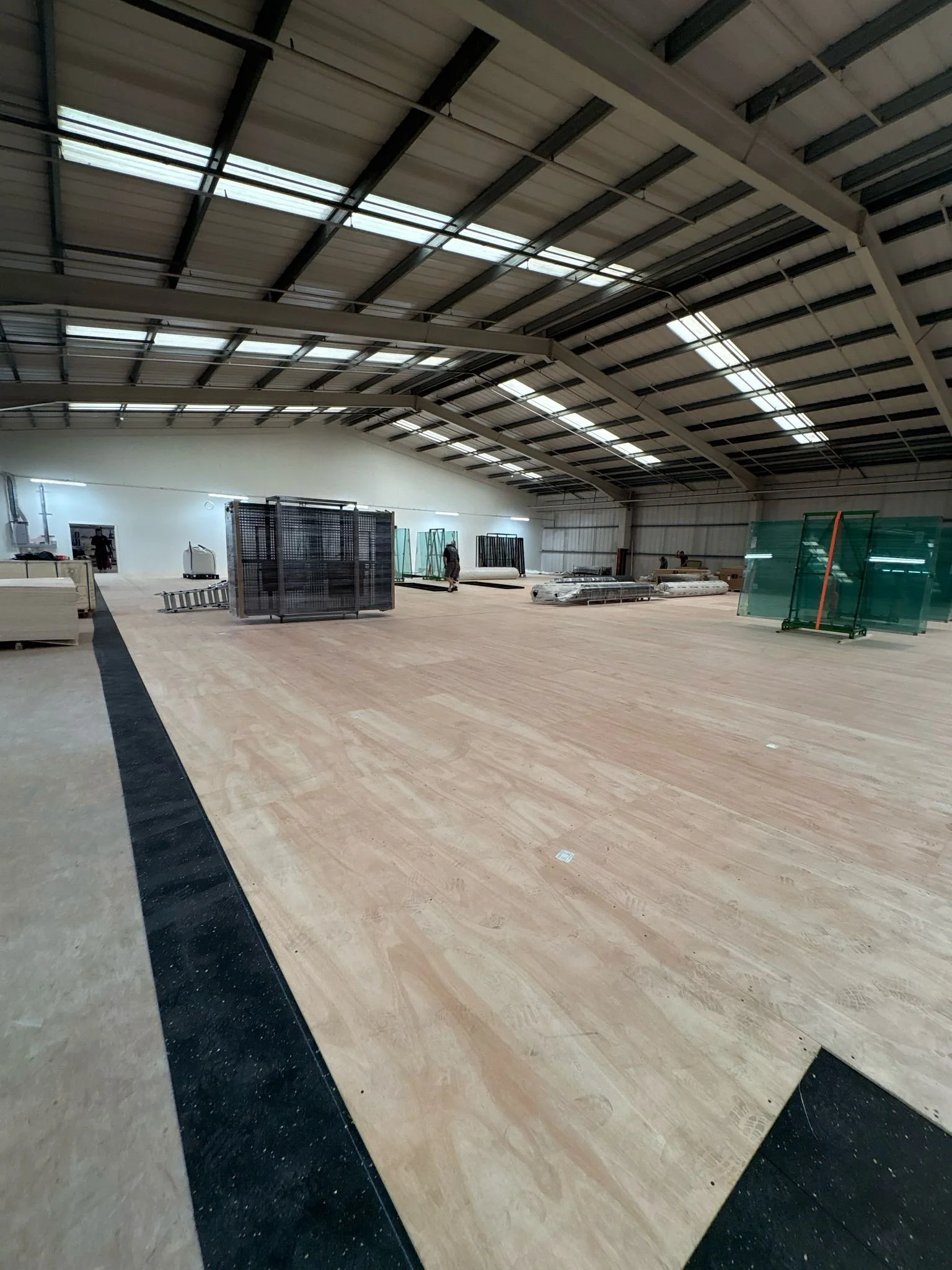 The image shows the interior of a large industrial or warehouse space under construction, with a high roof, skylights, and some workers and equipment scattered around being Prepared for Padel Court Installation.