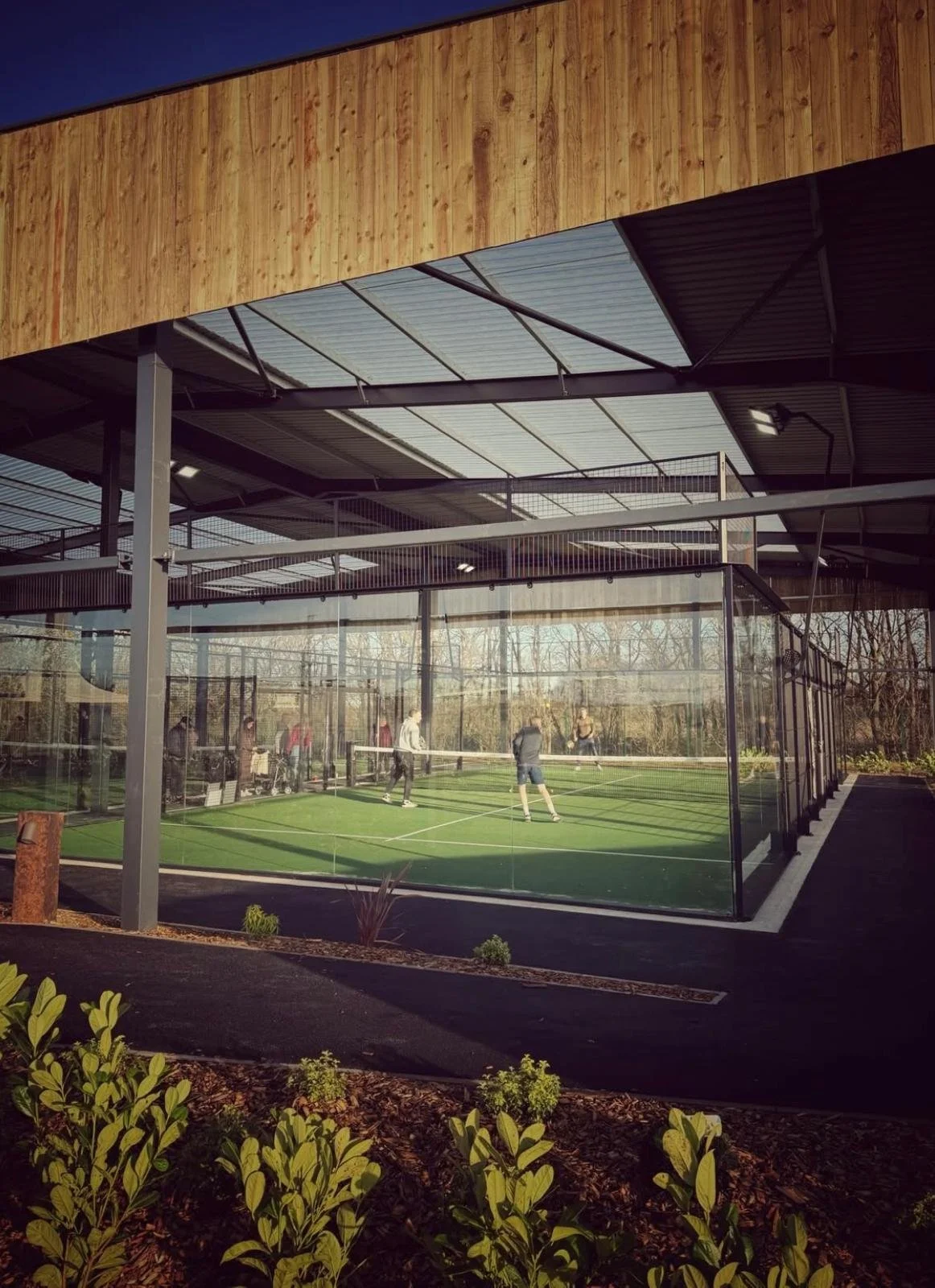 An indoor padel tennis court with glass walls and a Canopy.
