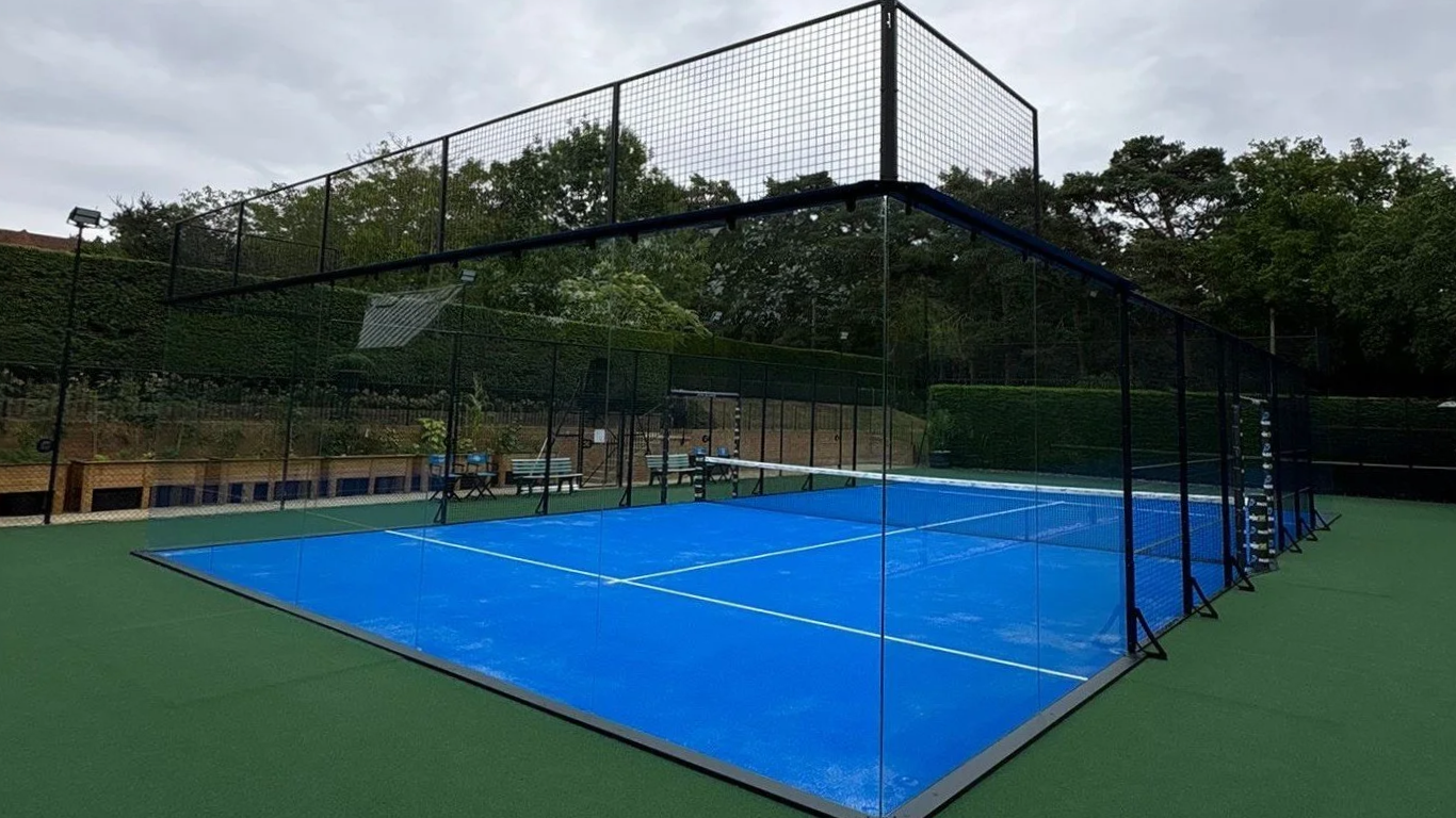 A private outdoor Fully Panoramic padel tennis court in the Uk. with green perimiter turf. No pillars in between the glass for 360 degree view