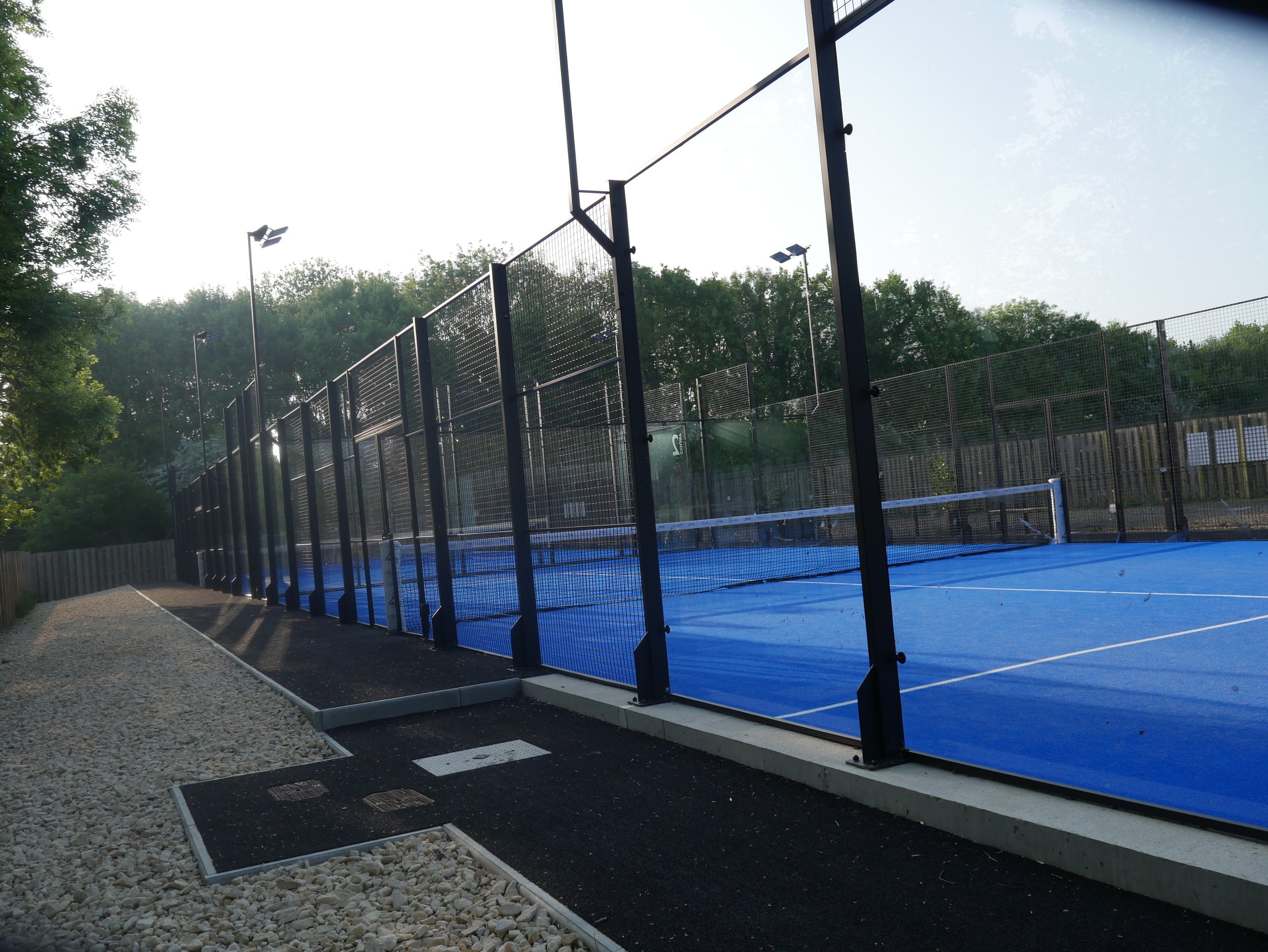 An outdoor Padel Court at the University of Cambridge with a walkway covered in black turf. UK Padel