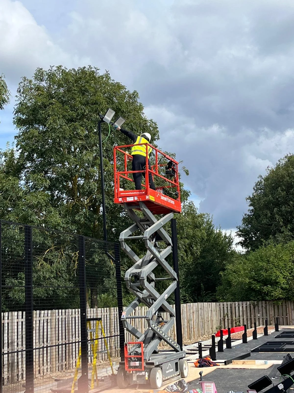 worker on a scissor lift rigging the lights for a Padel Court at the University of Cambridge.