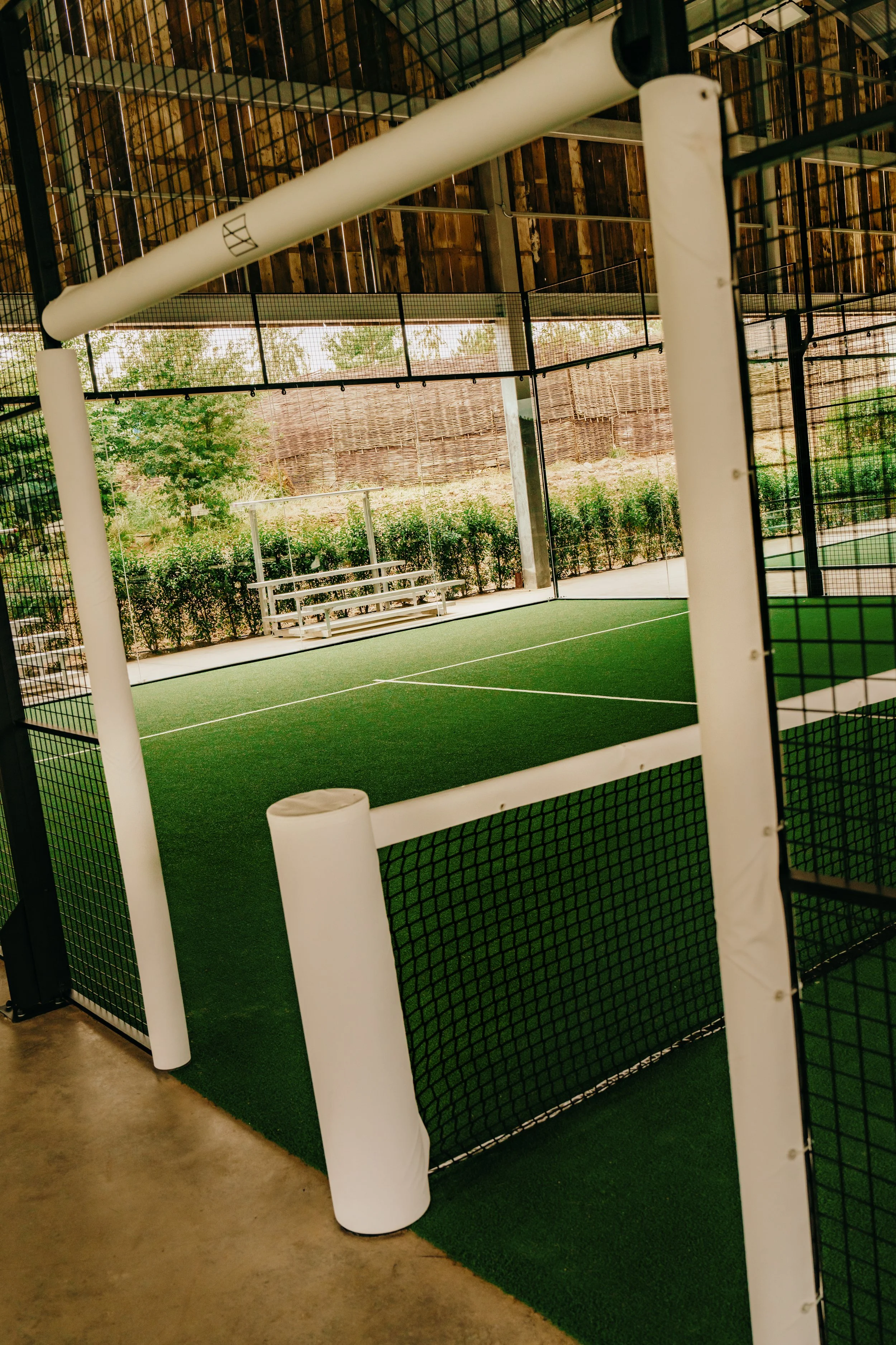 Indoor Padel court with green turf underneath a Canopy with natural outdoor scenery in the background.