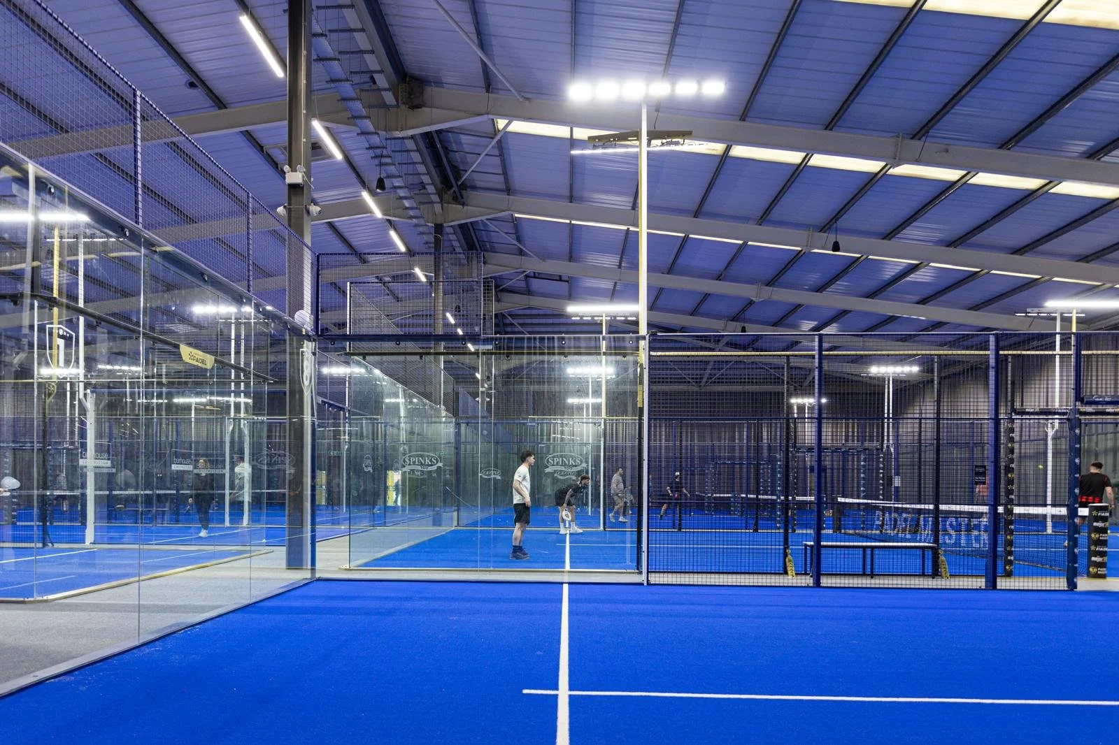 Indoor padel court with blue surface and glass walls, players practicing the game.