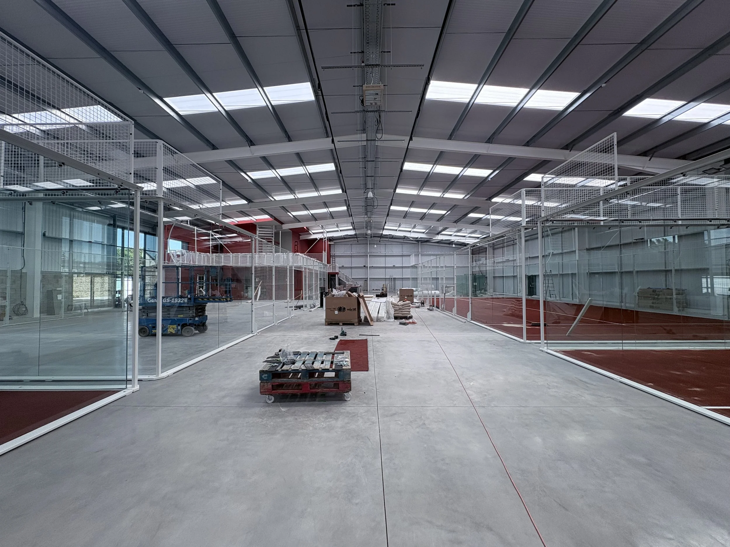 Construction site inside a large building with a high, curved ceiling, metal framework, and glass walls, with tools and construction materials scattered on the floor.