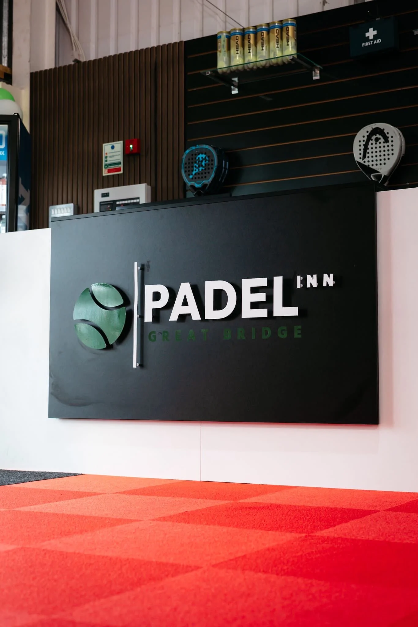 Entrance to the Padel Inn with the front desk, rackets and balls on the wall behind and a large sign that reads "padel Inn"