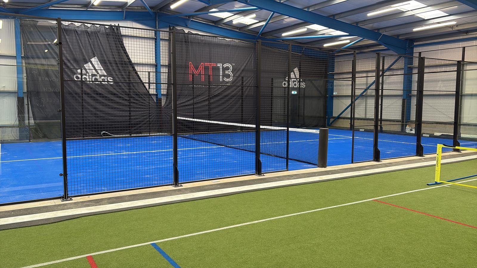 Indoor sports facility with a blue Padel court, with a multi sports area next to it. The Rally Hub Padel.