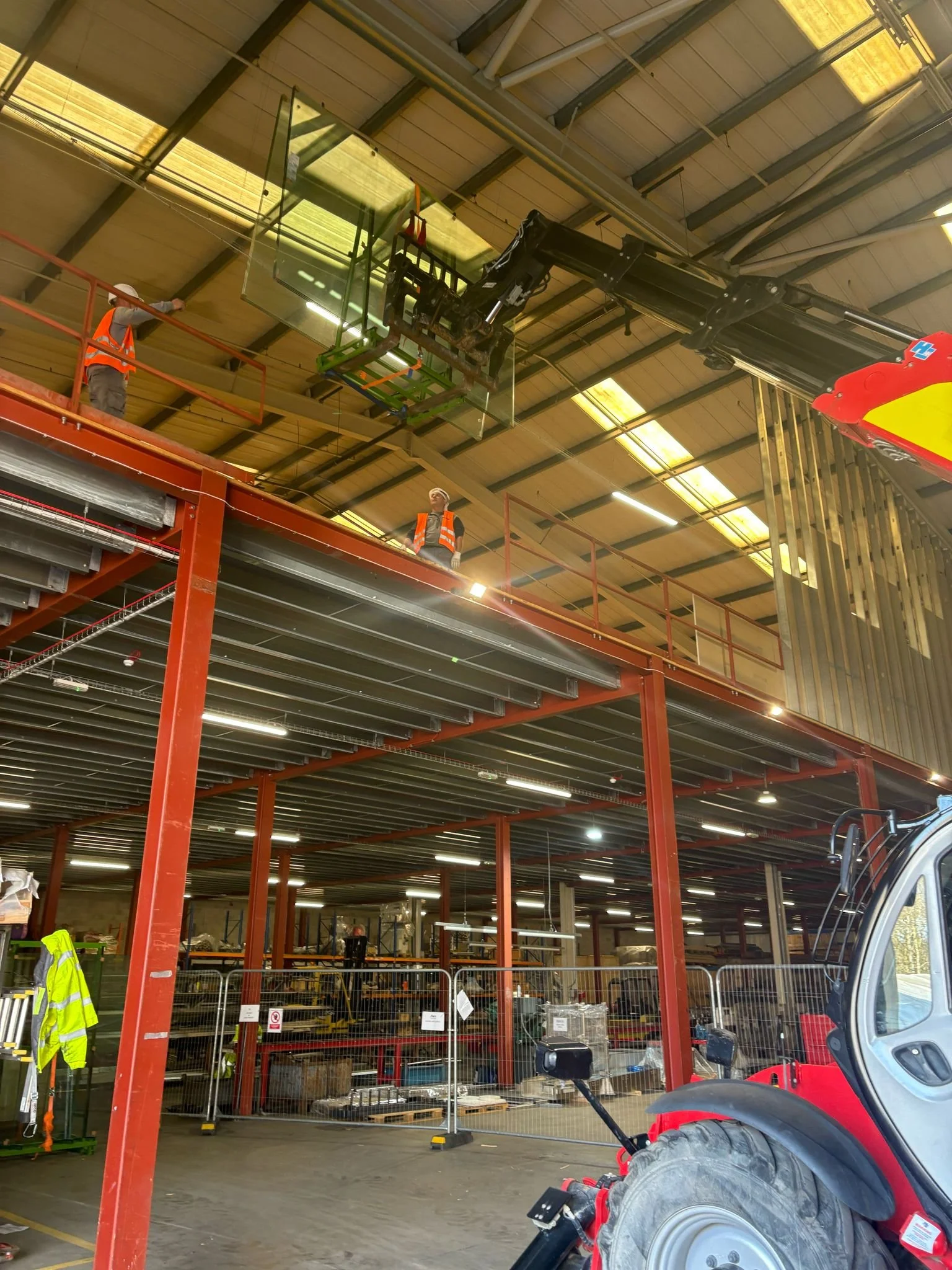 Construction workers installing a large glass panel on the ceiling inside a warehouse with red steel beams, guardrails, and Padel Court Materials.