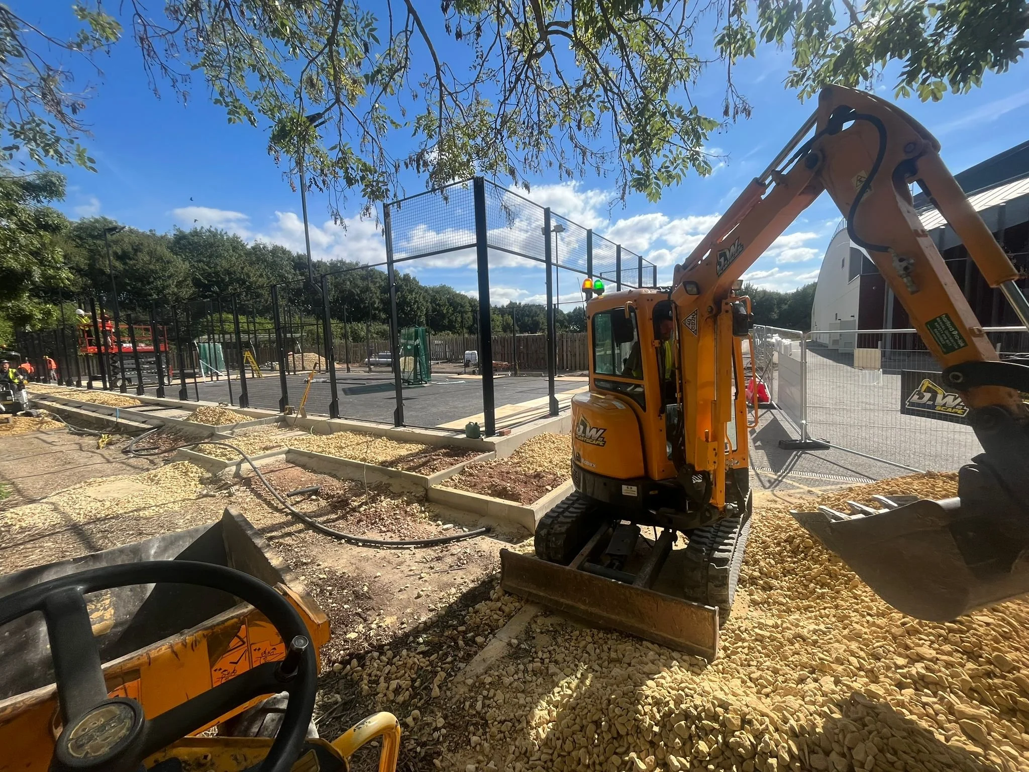 Padel Court Construction for the University of Cambridge. there is a digger. The path around the court is being built.