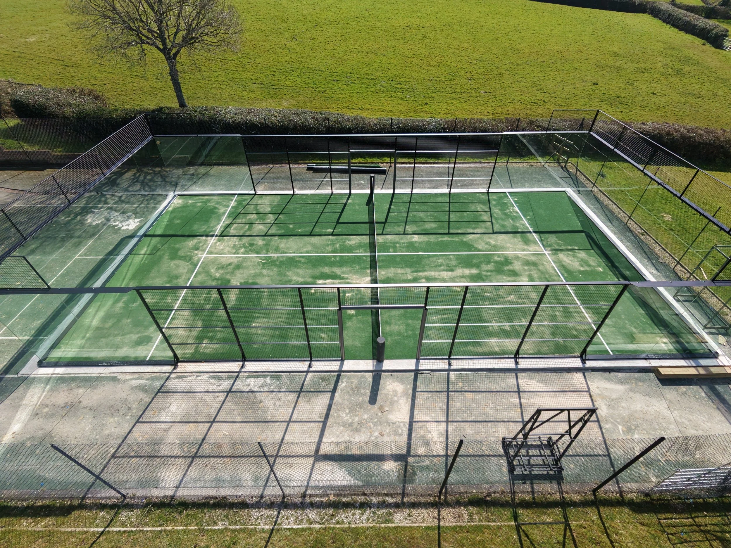 An aerial view of a private Padel court with green surface and surrounding grassy area.