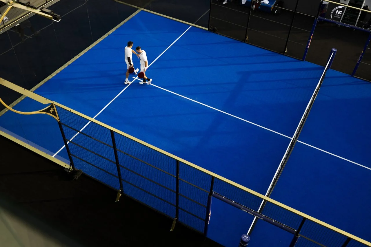 Two Padel Players on a Premier Padel Court. Blue turf with a Black and Gold Premium frame. During a Tournament. UK Padel.