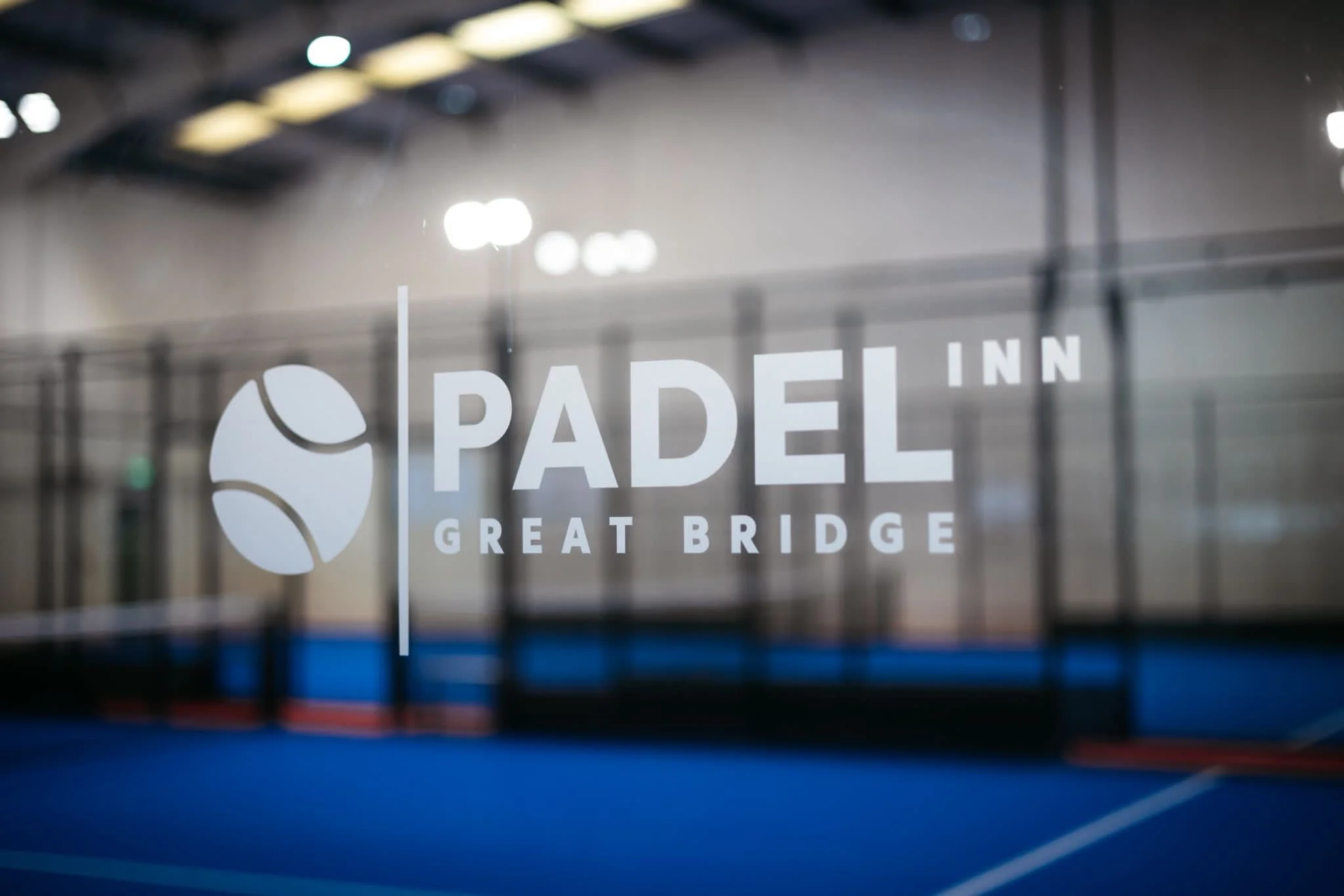 Glass window with the logo and name of Padel Great Bridge, Padel Venue visible in the reflection.