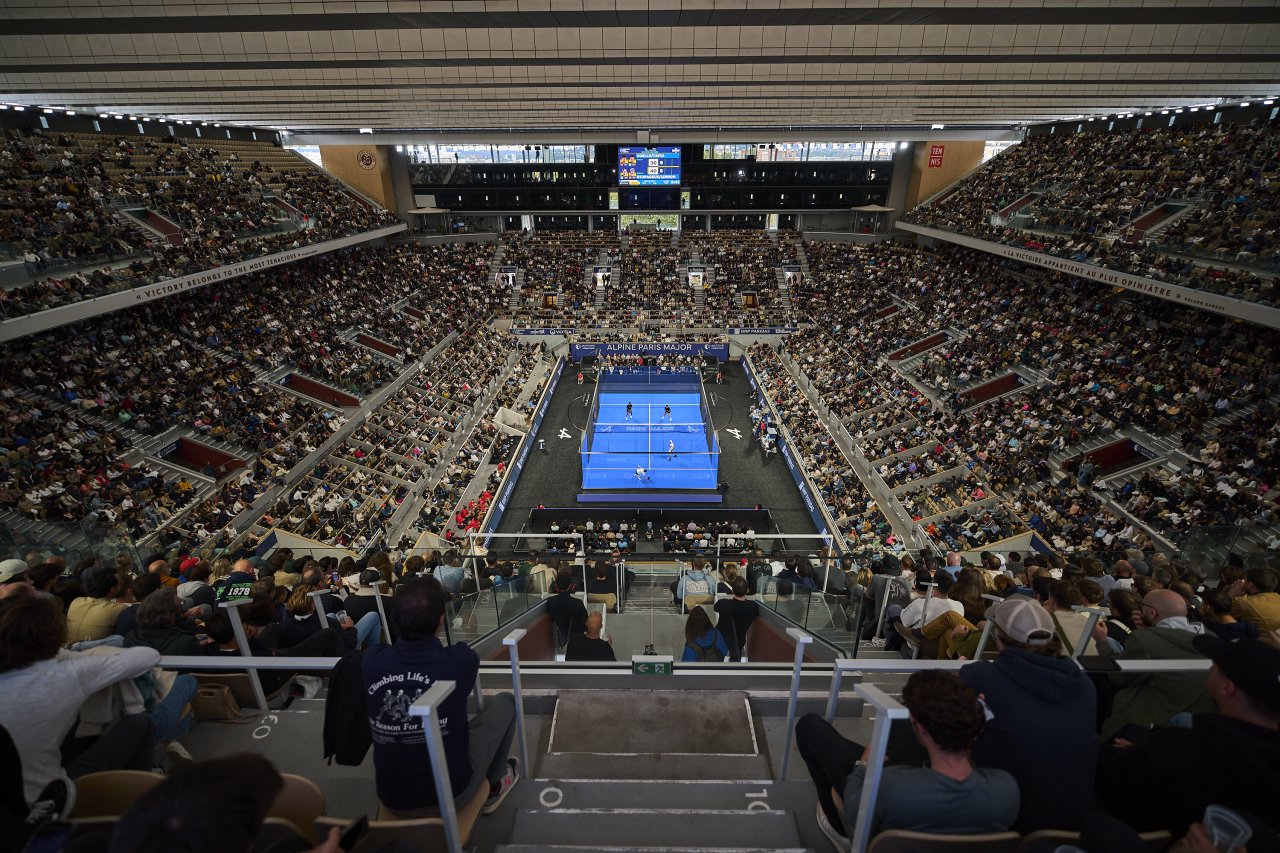Indoor Padel stadium filled with spectators watching a match on a blue court UK.
