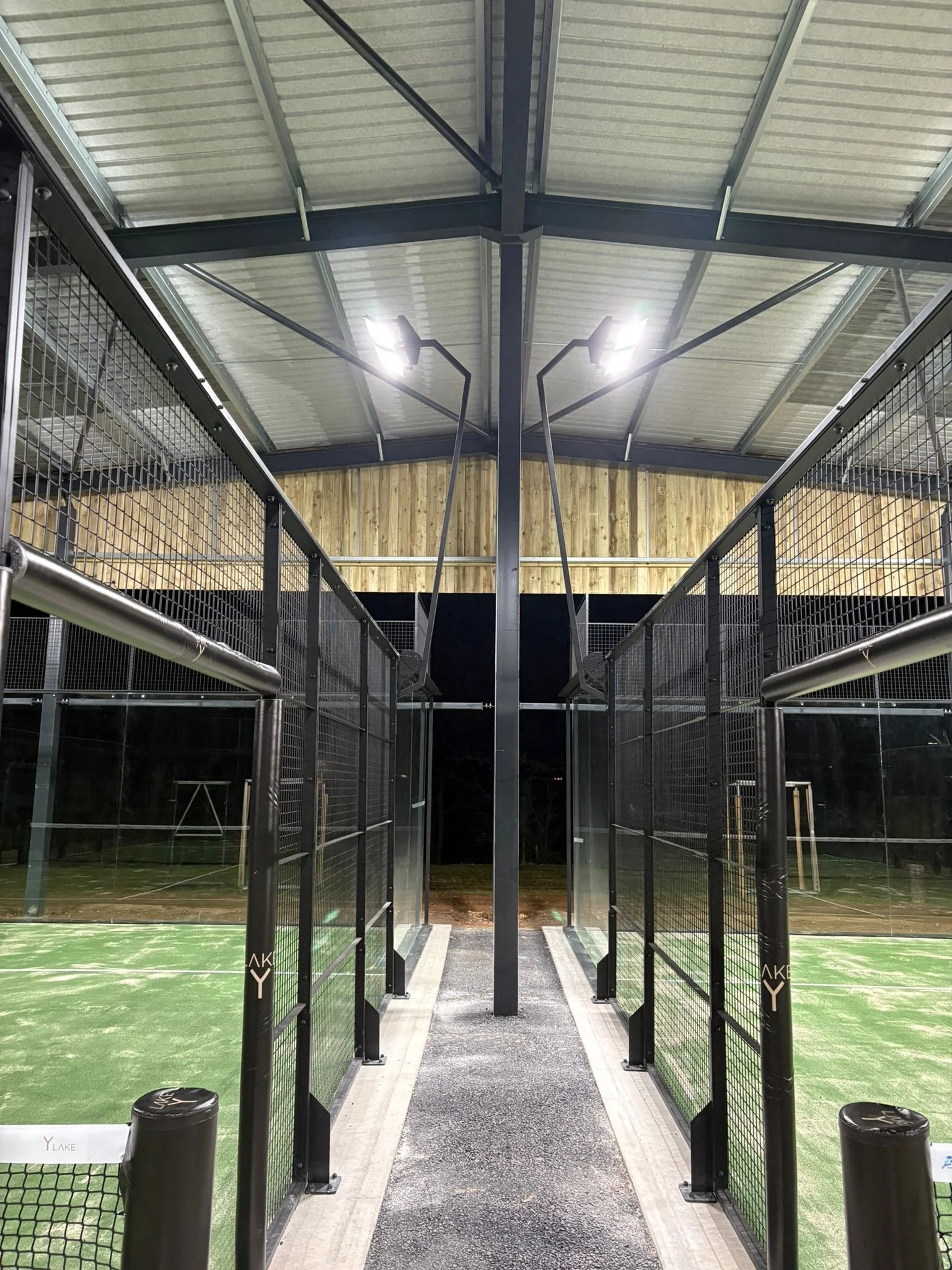 Indoor Padel Courts next to each other underneath a canopy with overhead lighting.