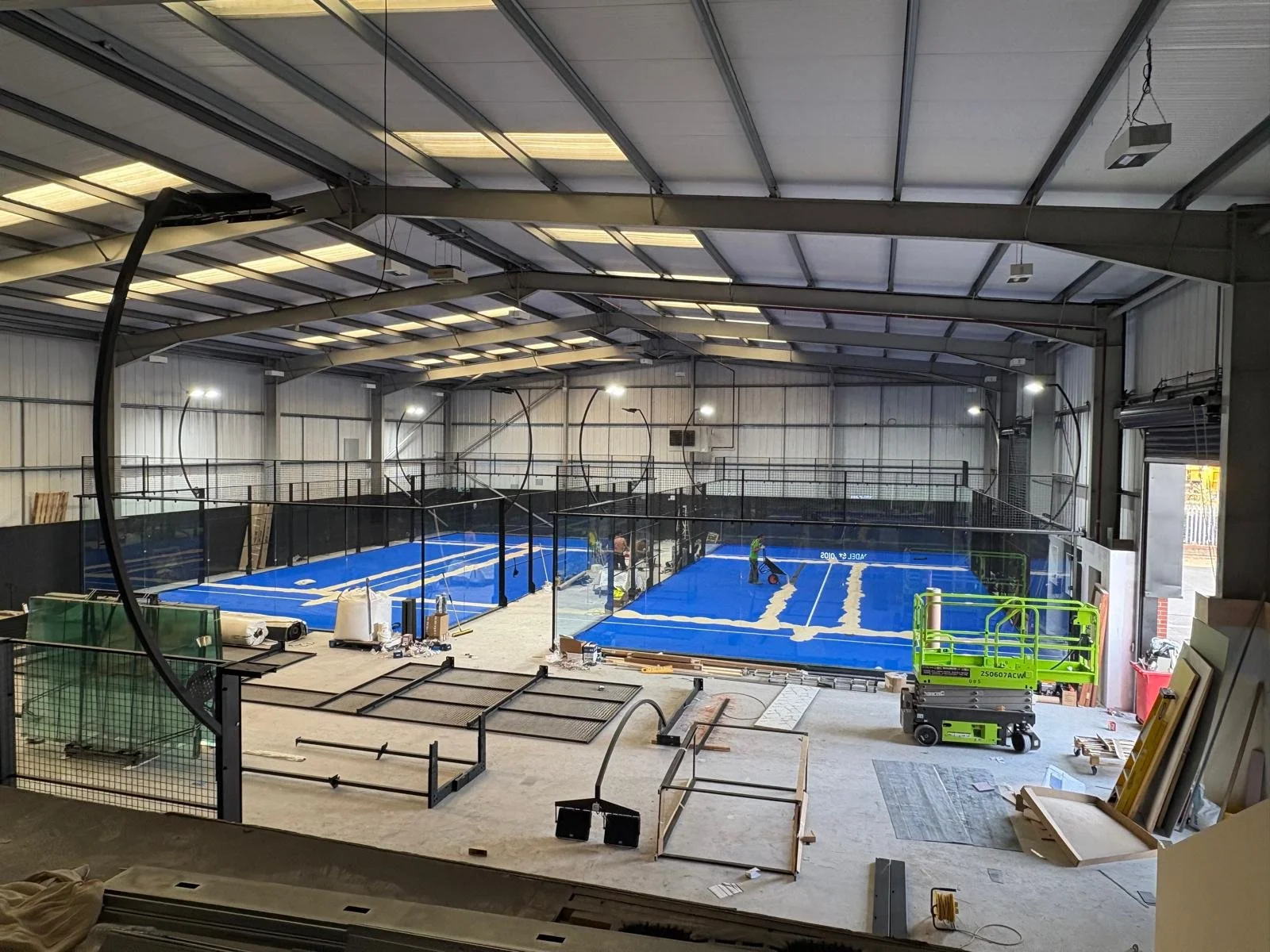 Indoor UK sports facility under construction with multiple blue Padel Courts, construction equipment and materials around.