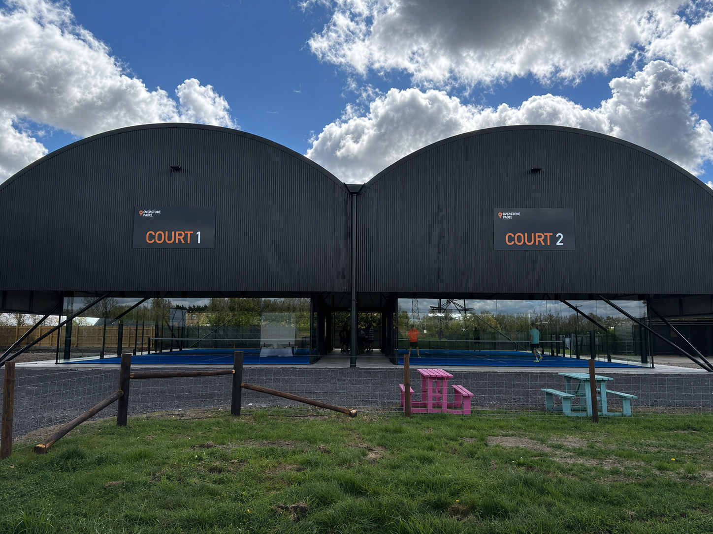 Outdoor sports complex with two enclosed padel courts labeled 'Court 1' and 'Court 2' under a partly cloudy sky.