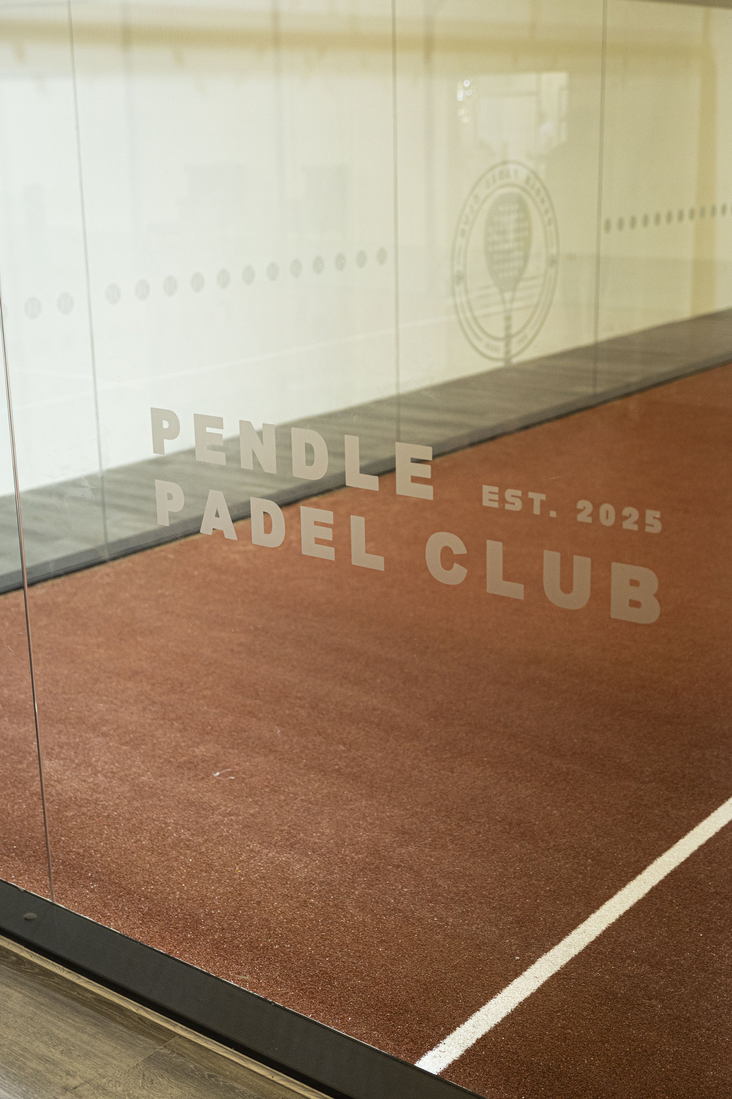 A Padel Court with the words "PENDLE PADEL CLUB" and "EST. 2025" written on the glass, with Red Terracotta turf