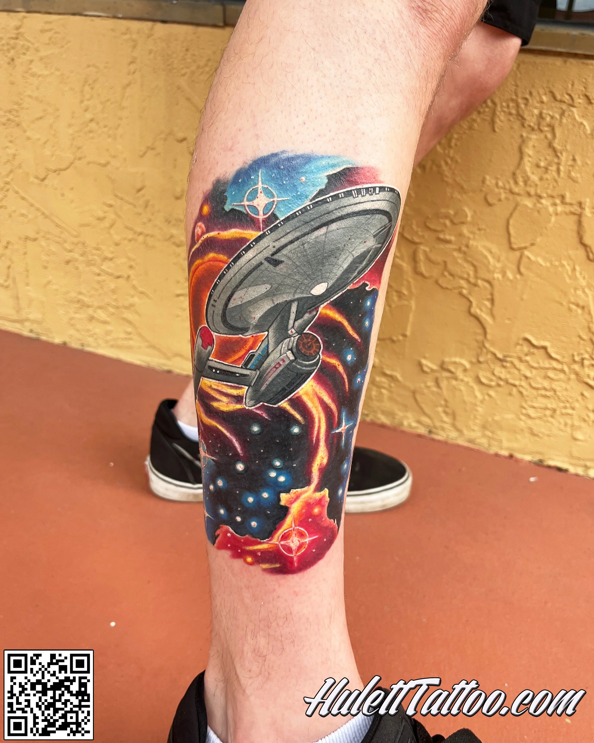 Colorful tattoo of the USS Enterprise from Star Trek flying through space, with planets and stars in the background.