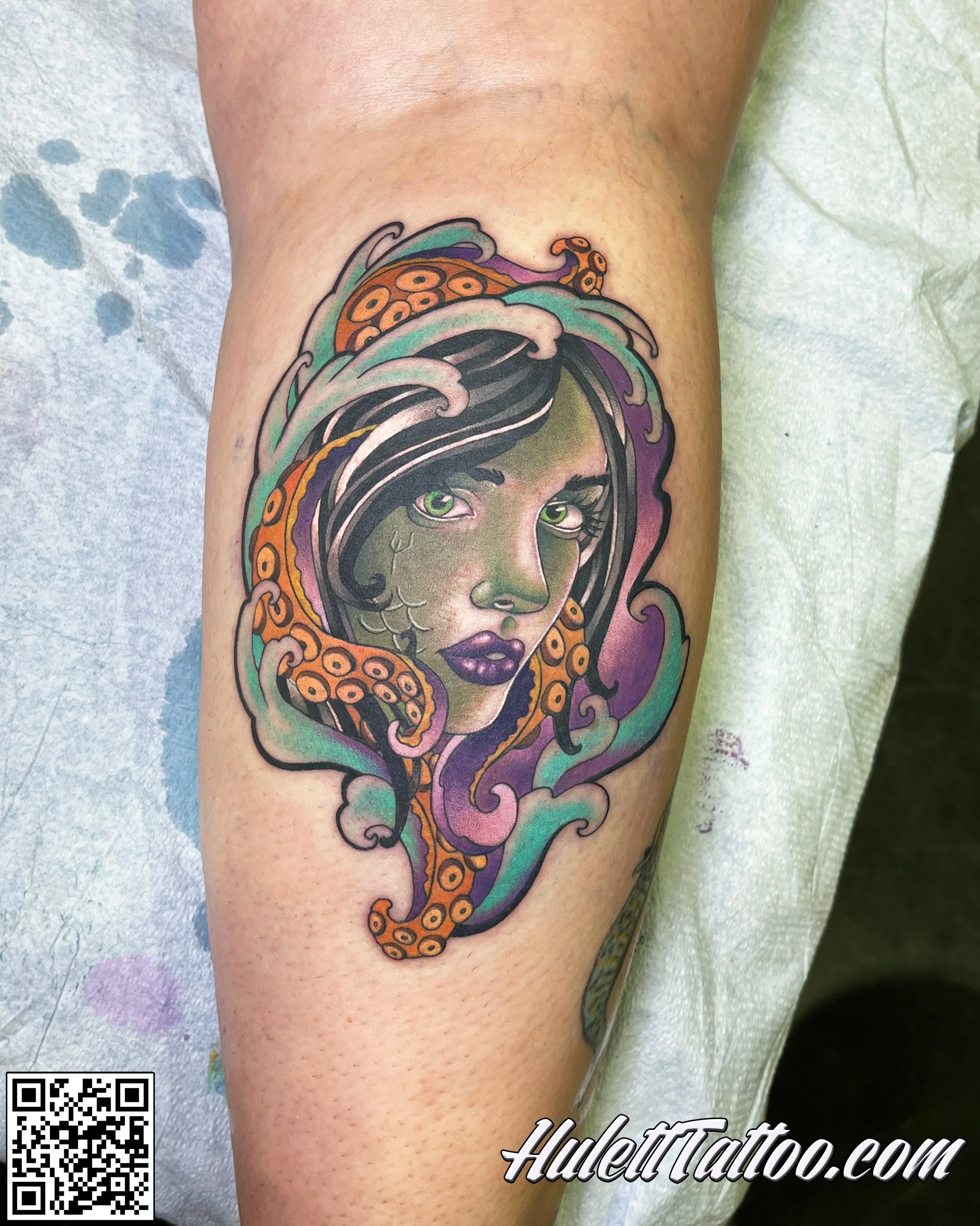 Tattoo of a woman with green eyes and purple lips, with sea waves and octopus tentacles surrounding her face.