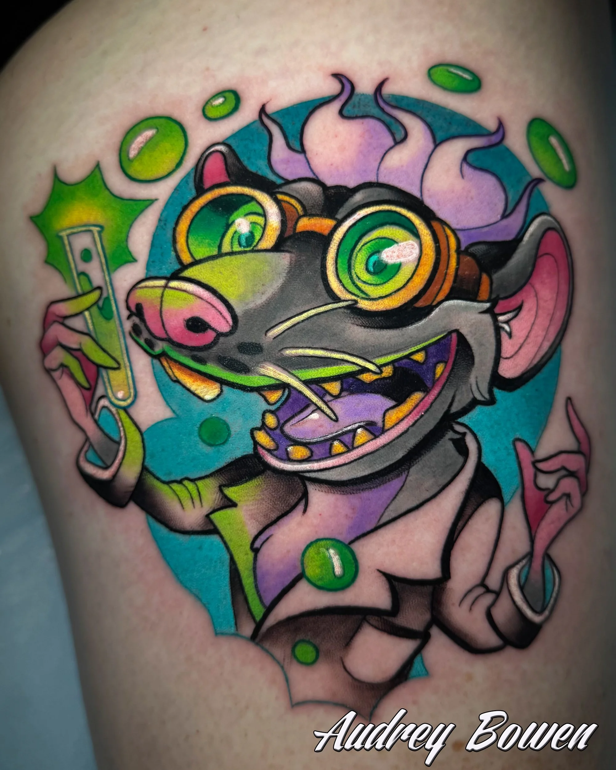 Colorful tattoo of mad scientist rat with vortex eyes, green background, purple spines, and a mischievous expression. Tattoo by Audrey Bowen, Karmic Tattoo, Clearwater Florida
