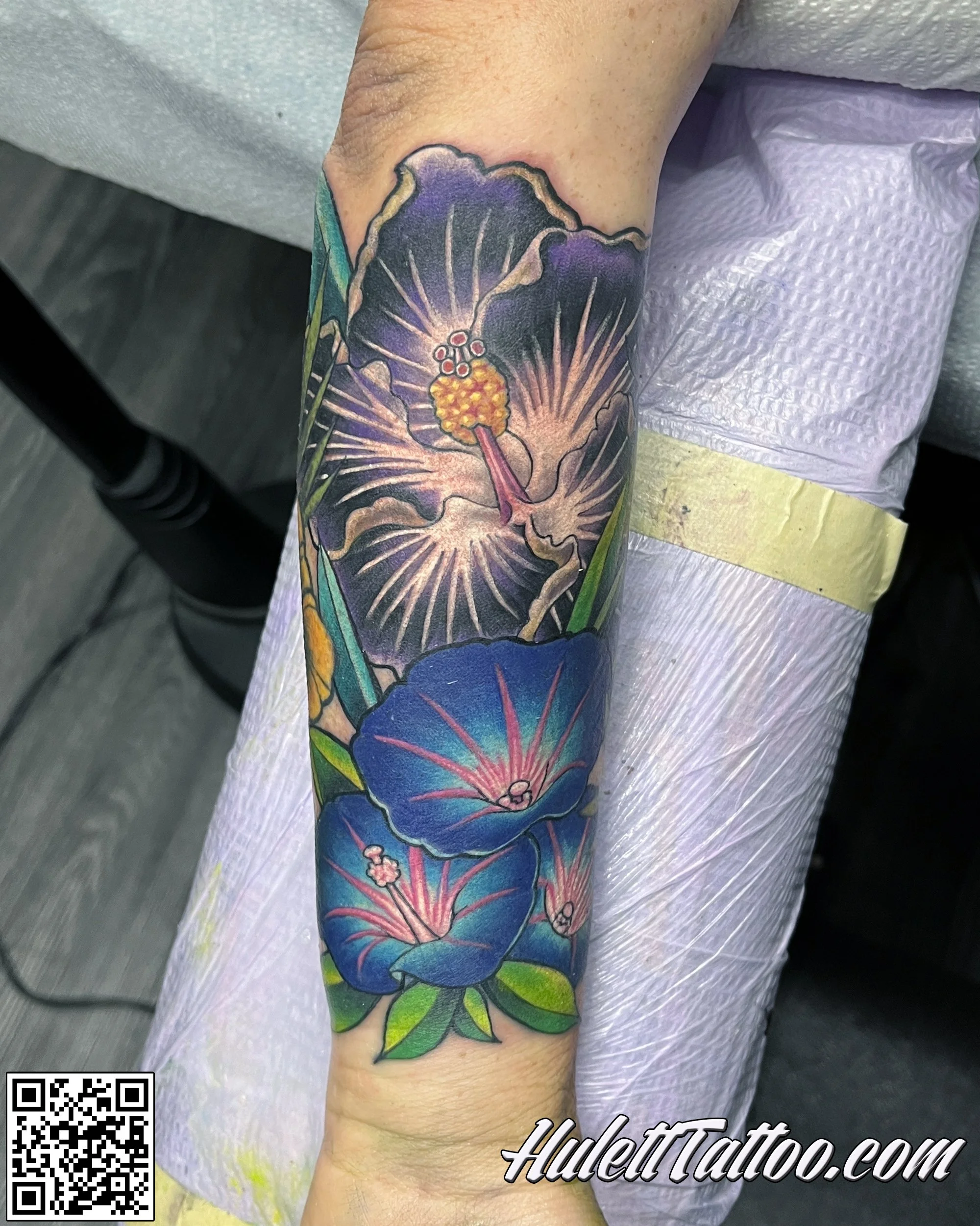 A colorful tattoo of purple morning glories with green leaves on a person's forearm.