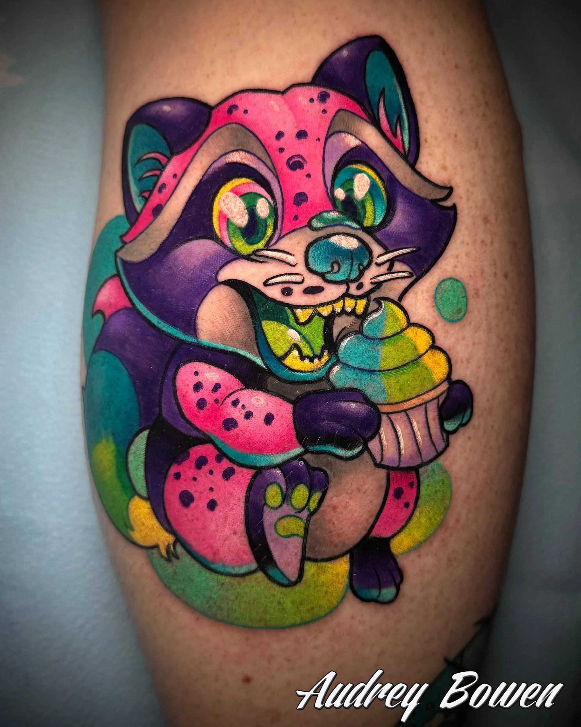 Colorful tattoo of a stylized racoon, with large expressive eyes, vibrant pink, purple, teal, and yellow colors, and detailed features. Tattoo by Audrey Bowen, Karmic Tattoo, Clearwater Florida