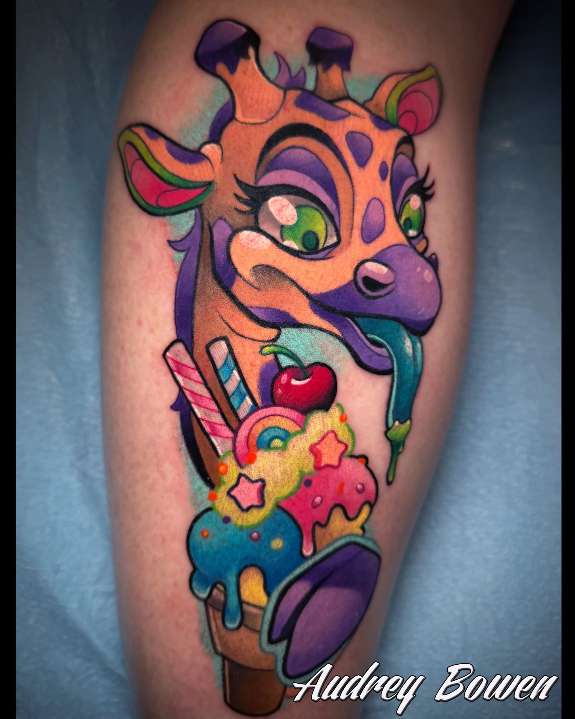 Colorful tattoo of a cartoon giraffe with large green eyes, surrounded by rainbow-colored clouds and stars. Tattoo by Audrey Bowen, Karmic Tattoo, Clearwater Florida