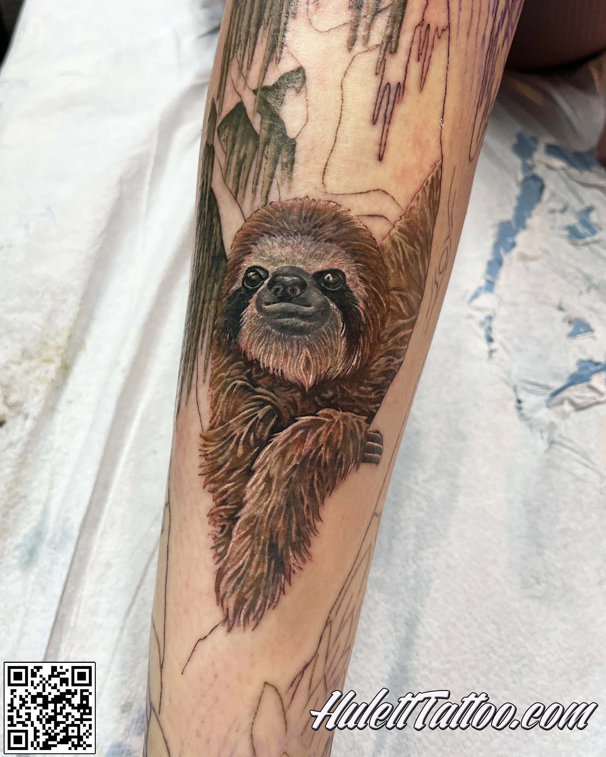 Close-up of a tattoo on a person's leg, depicting a sloth in a realistic style with detailed fur, and a background with lines and shapes, partially obscured by a watermark reading 'Huletttattoo.com' and a QR code.