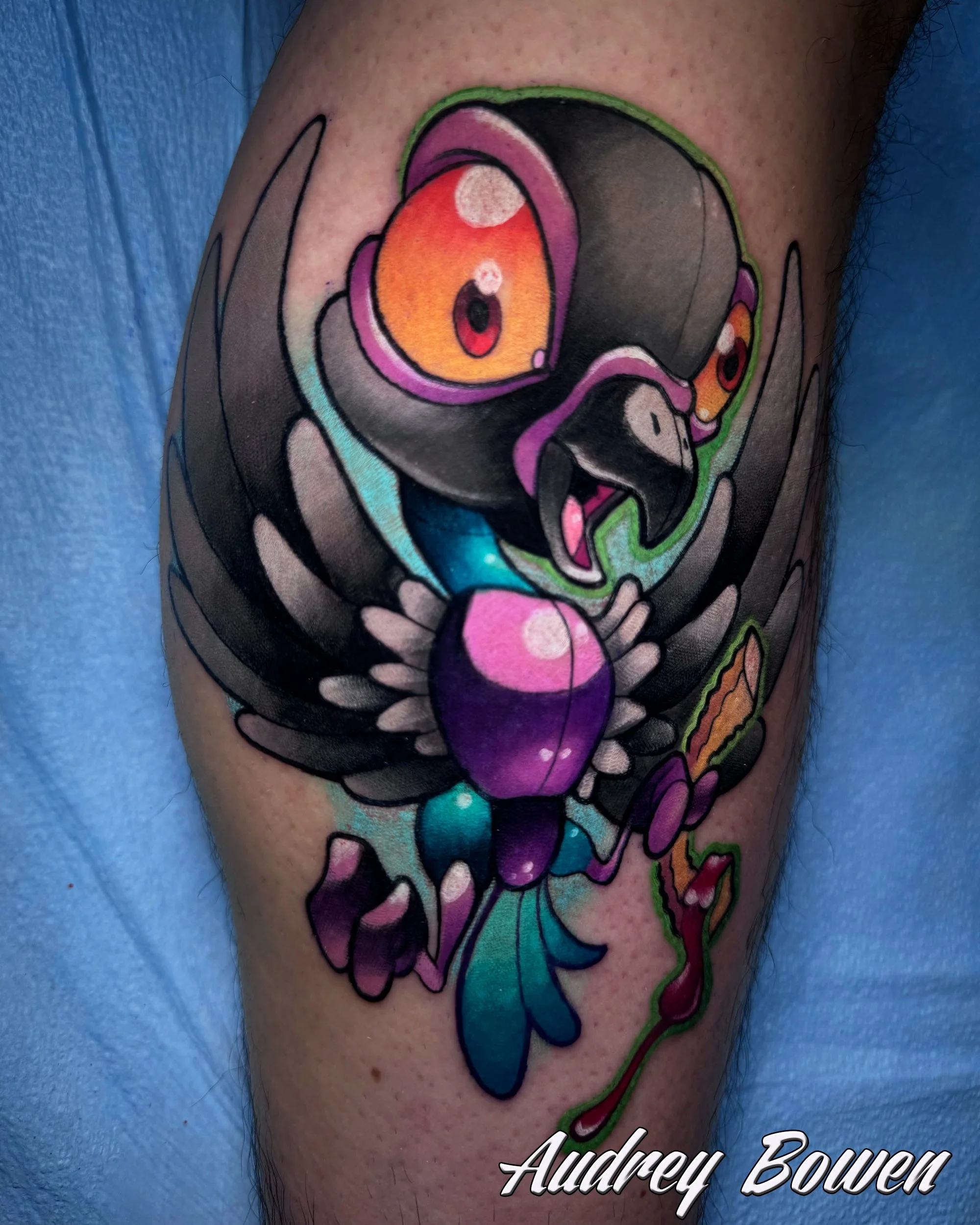 Colorful tattoo of a new school parrot with large eyes, bold outlines, and vibrant colors on a person's arm. Tattoo by Audrey Bowen, Karmic Tattoo, Clearwater Florida