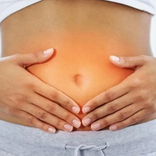 Close-up of a person's bare abdomen with hands resting on the stomach, wearing gray pants.