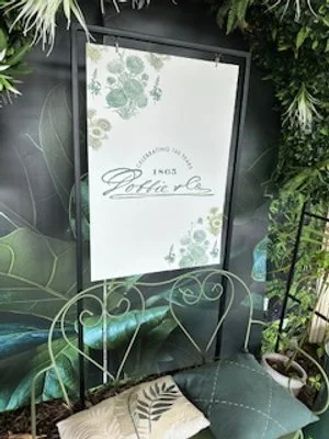 Indoor floral sign display with greenery and decorative pillows on a metal chair.