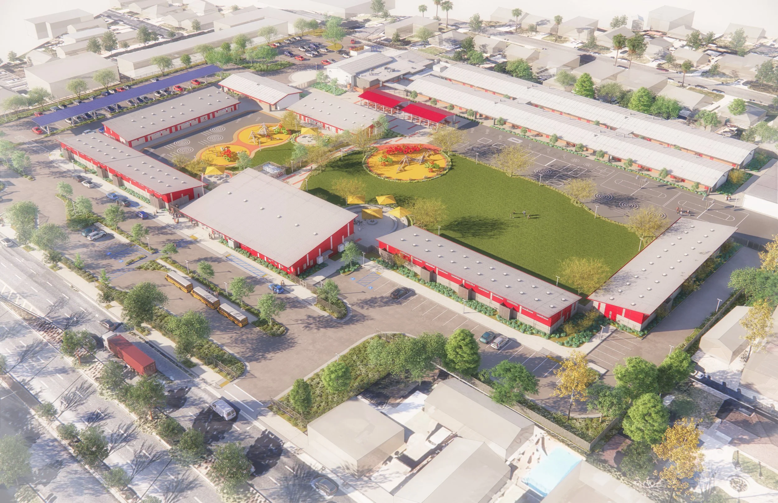 Aerial view of a school campus featuring multiple red buildings around a large grassy field, playground areas, parking lots with cars, and surrounding residential neighborhood with trees.