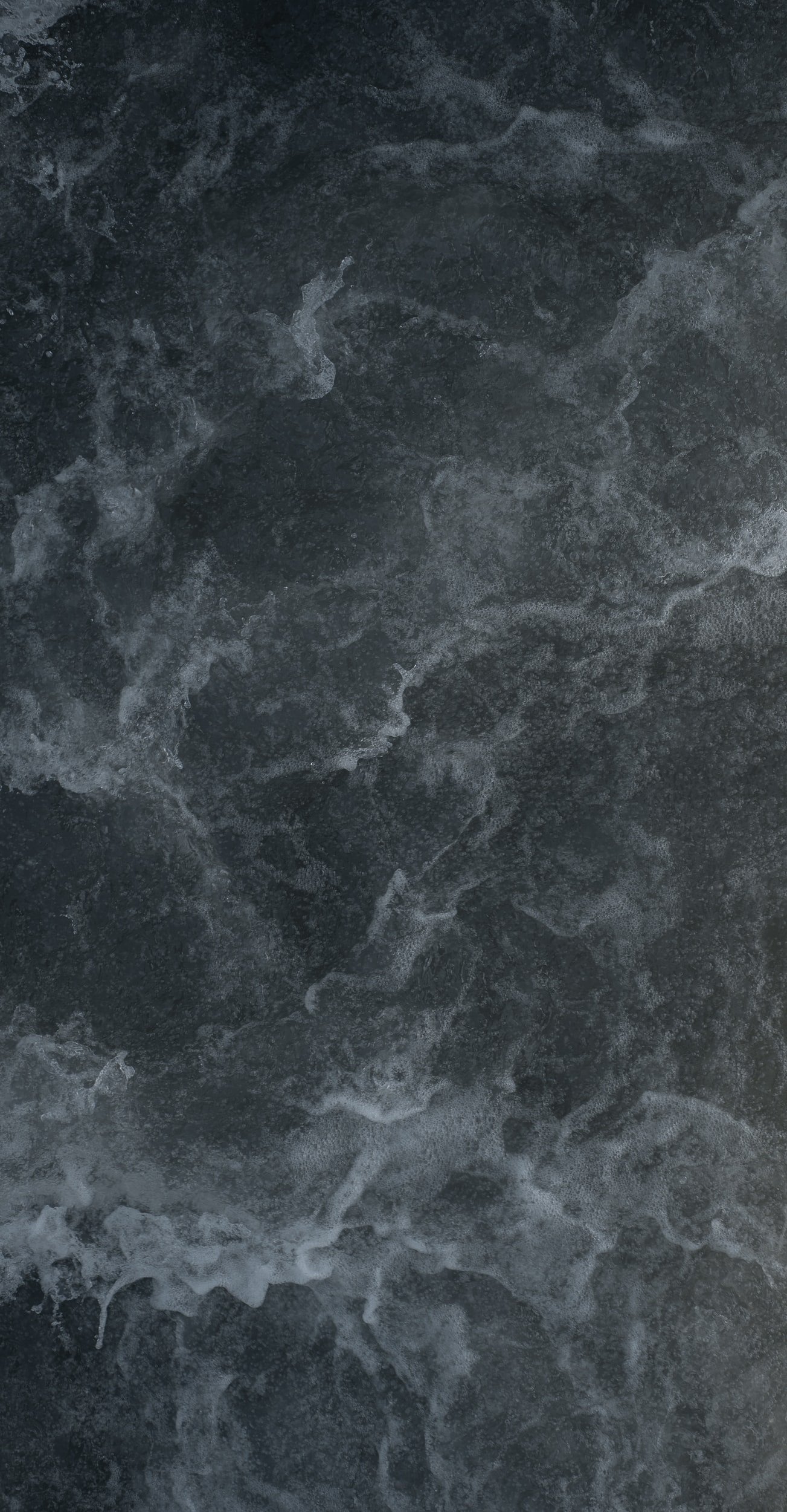 Close-up of ocean waves with foam and bubbles on the dark water surface.