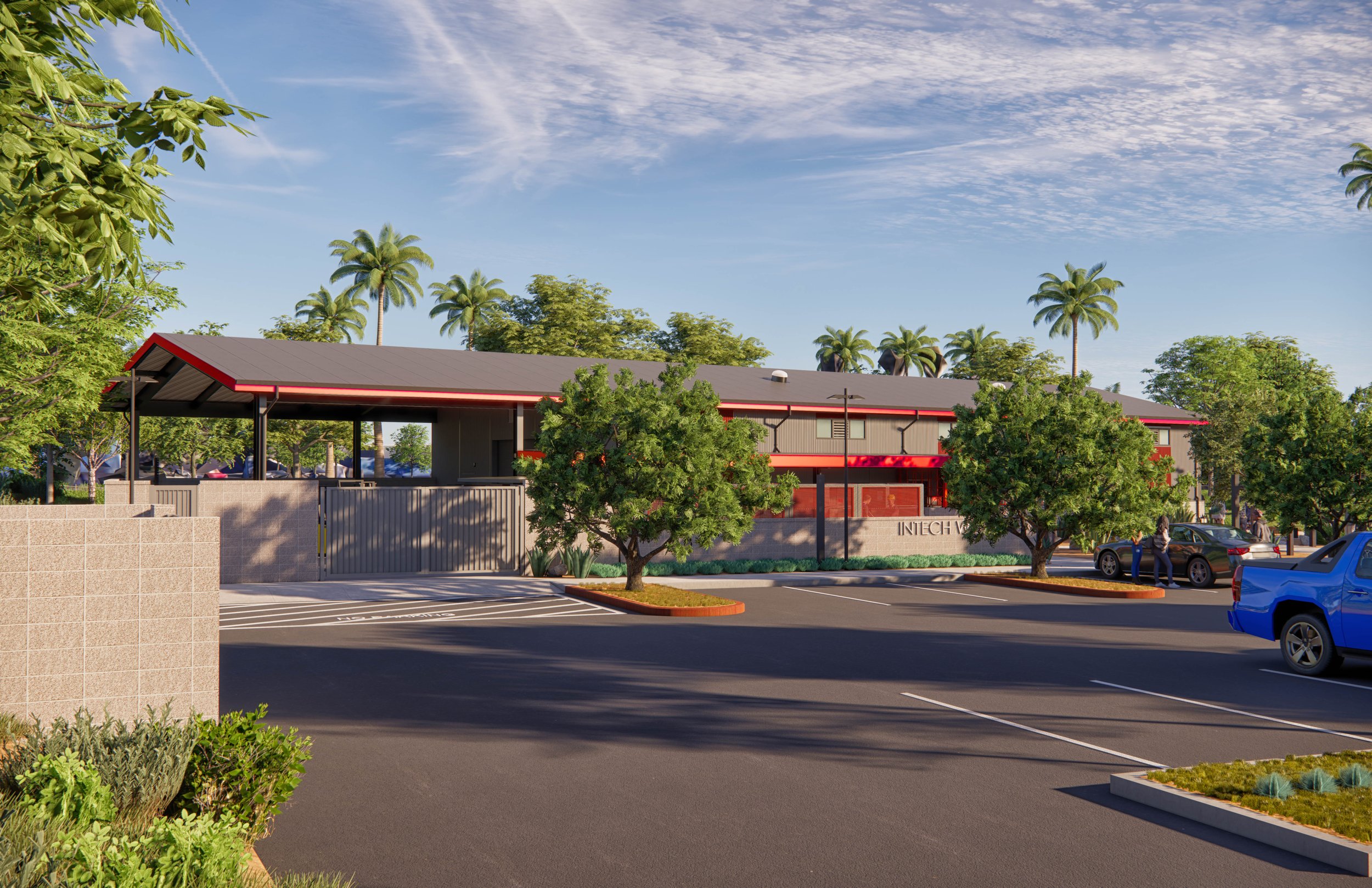 A parking lot with a few cars parked, green trees, and a building with a grey roof and red accents in the background under a partly cloudy sky.