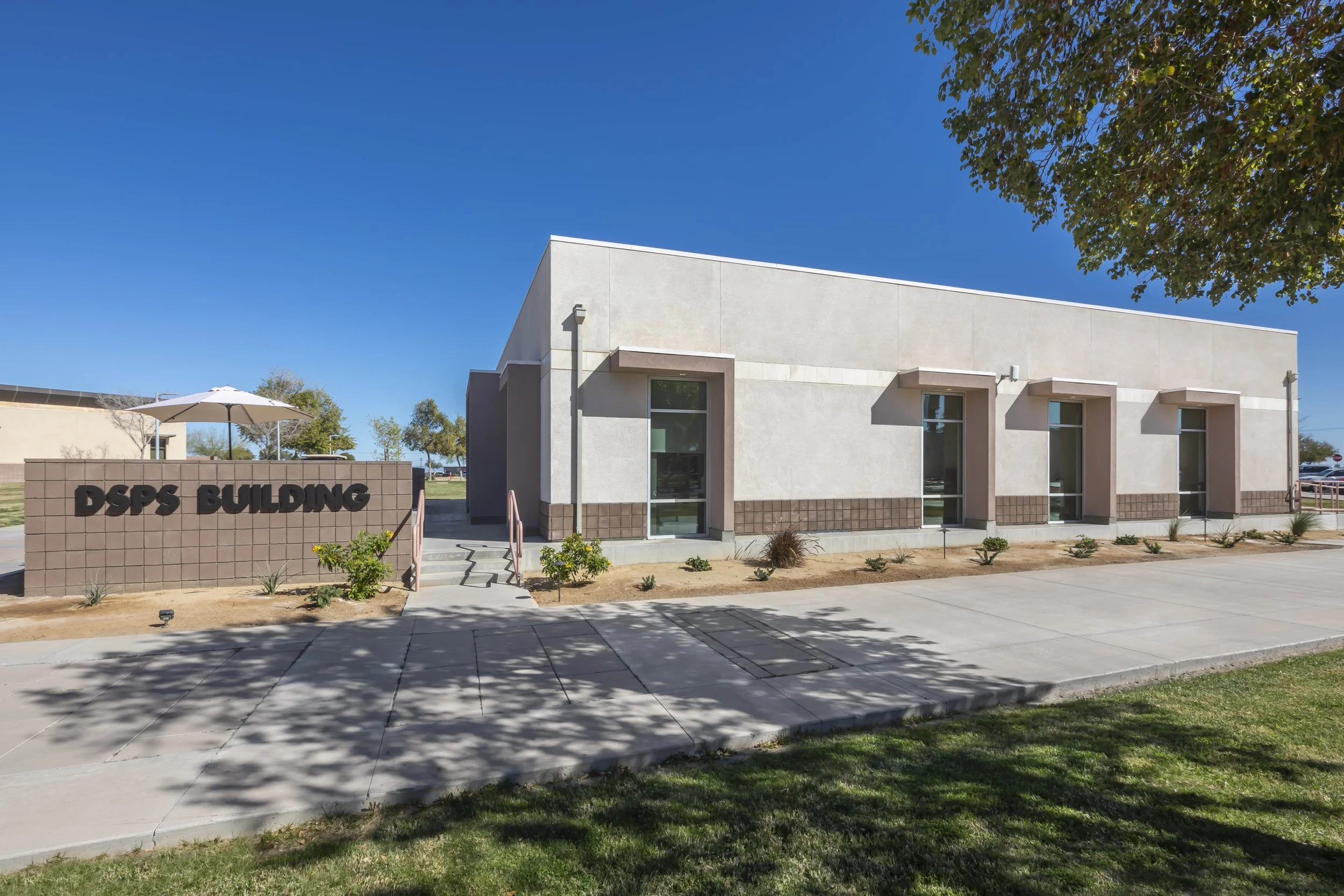 Exterior of a modern building identified as DSPS Building with a sign and landscaped front area under a clear blue sky.
